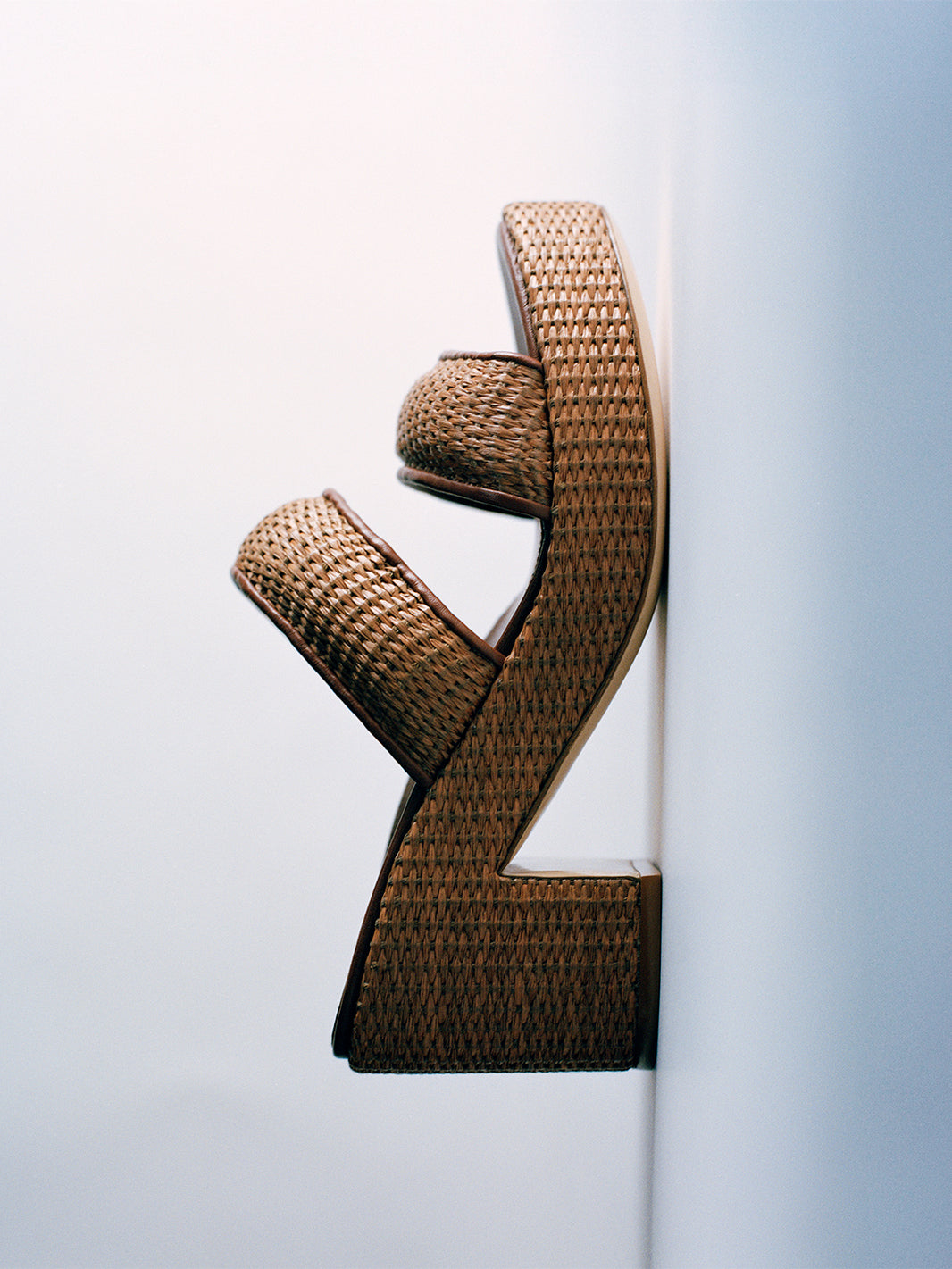 Profile view of a dark brown raffia platform sandal with a  leather trim and puffed straps. 