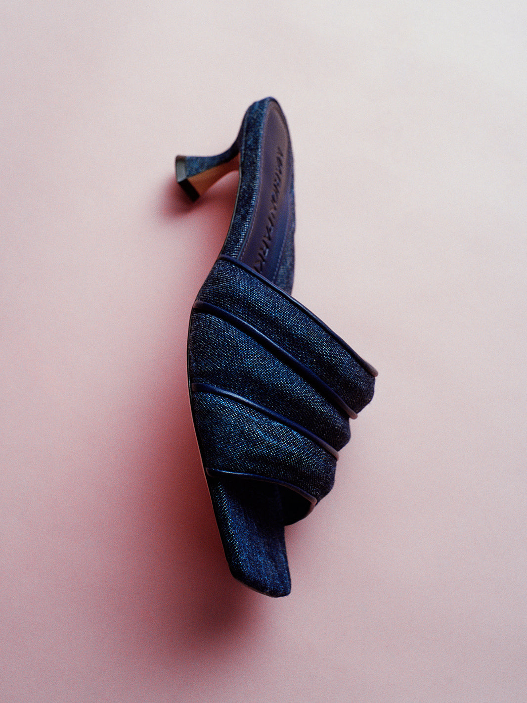 Profile view of a blue denim slide kitten heel with a leather trimed puffy strap detail.