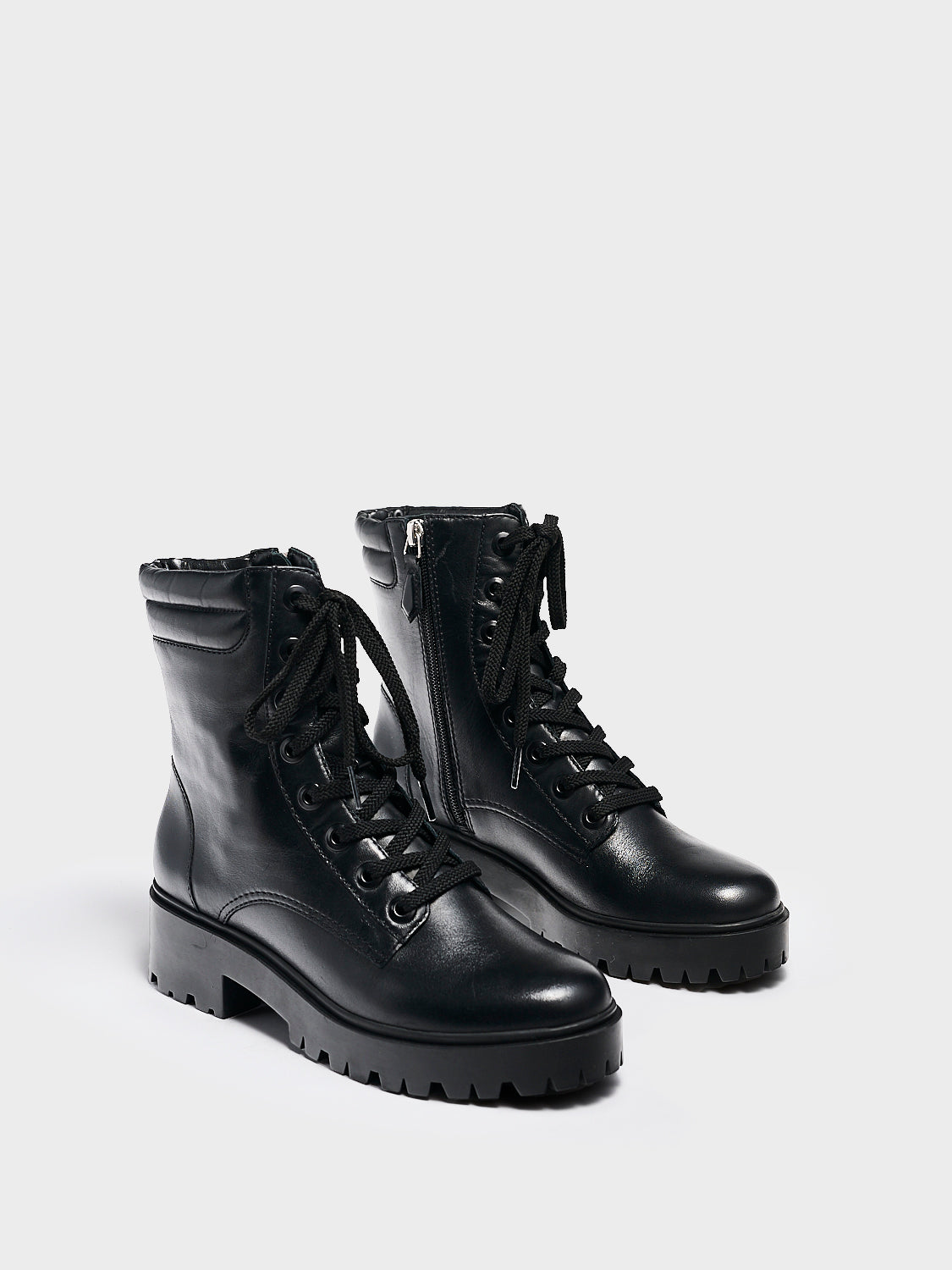 Angle view of a pair of black nappa leather lace-up boots with a lug sole, zipper closure, and round toe. 