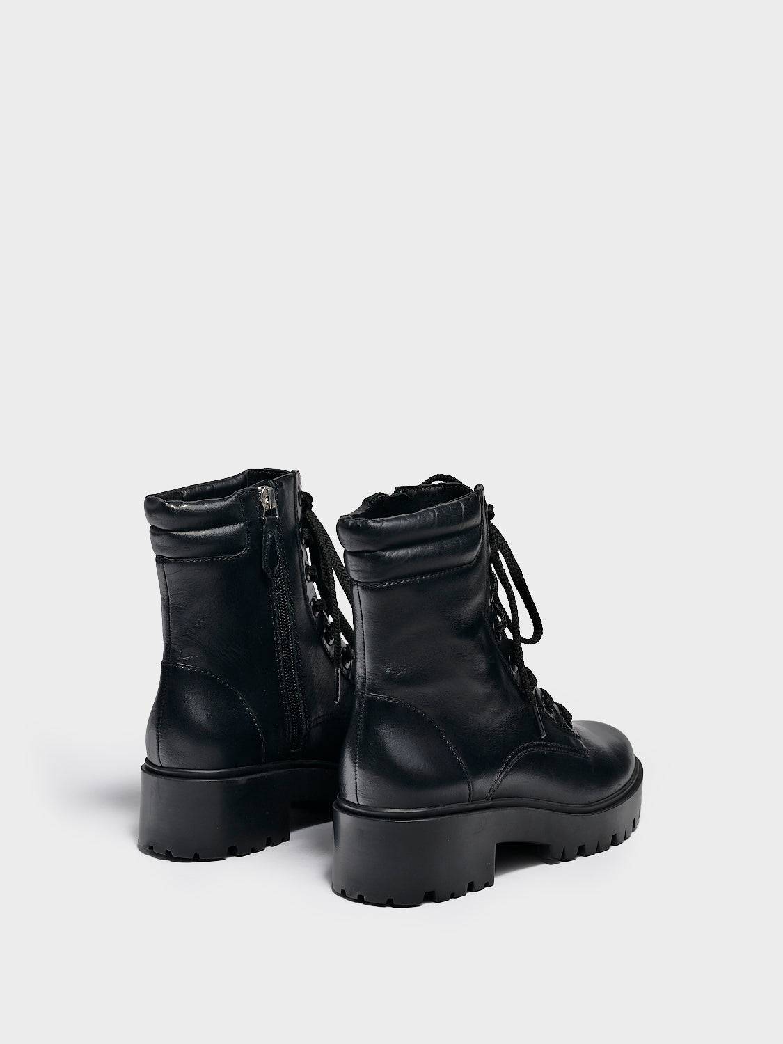 Back view of a pair of black nappa leather lace-up boots with a lug sole, zipper closure, and round toe. 