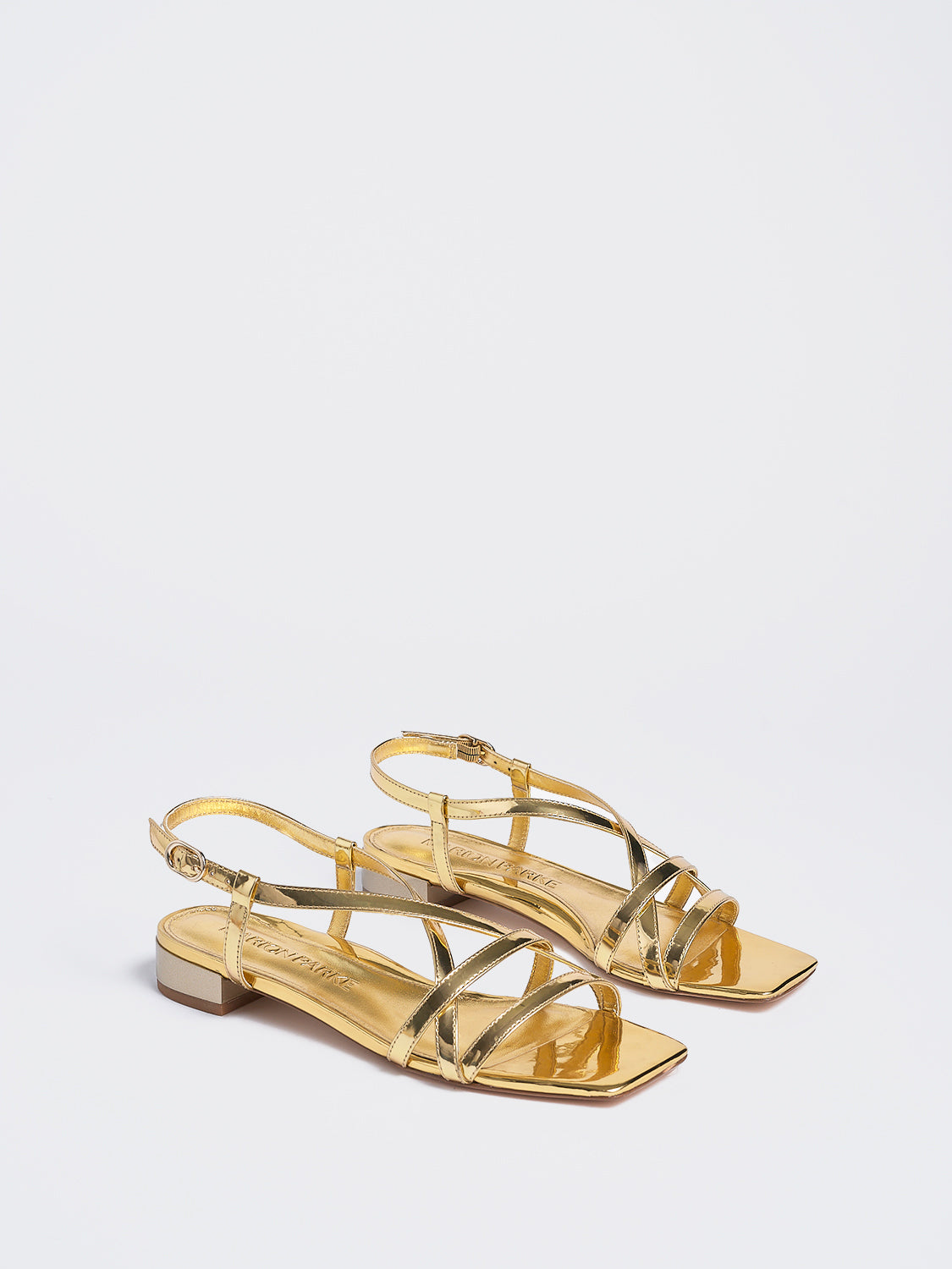 Angle view of a pair of gold metallic leather flat strappy sandals.