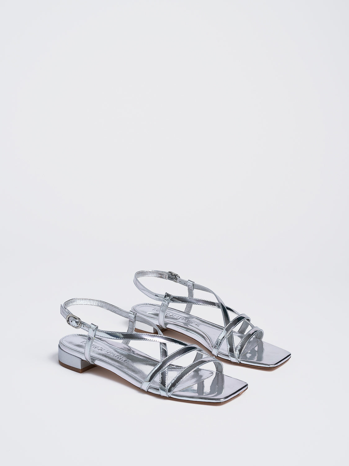 Angle view of a pair of silver metallic leather flat strappy sandals.
