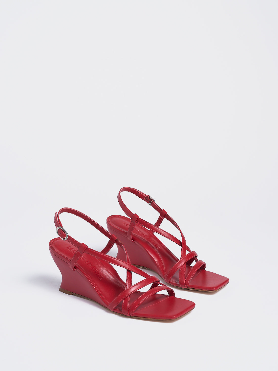 Angle view of a pair of lipstick red leather strappy sandals with a sculptural wedge.