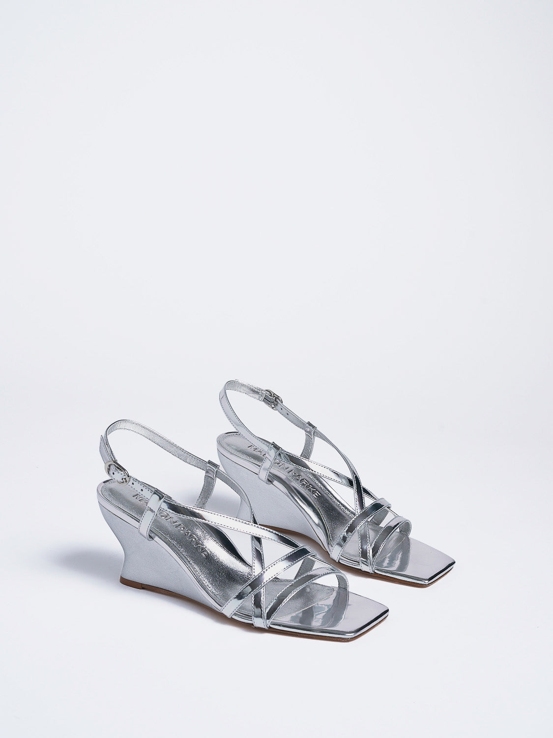 Angle view of a pair of silver metallic leather strappy sandals with a sculptural wedge.