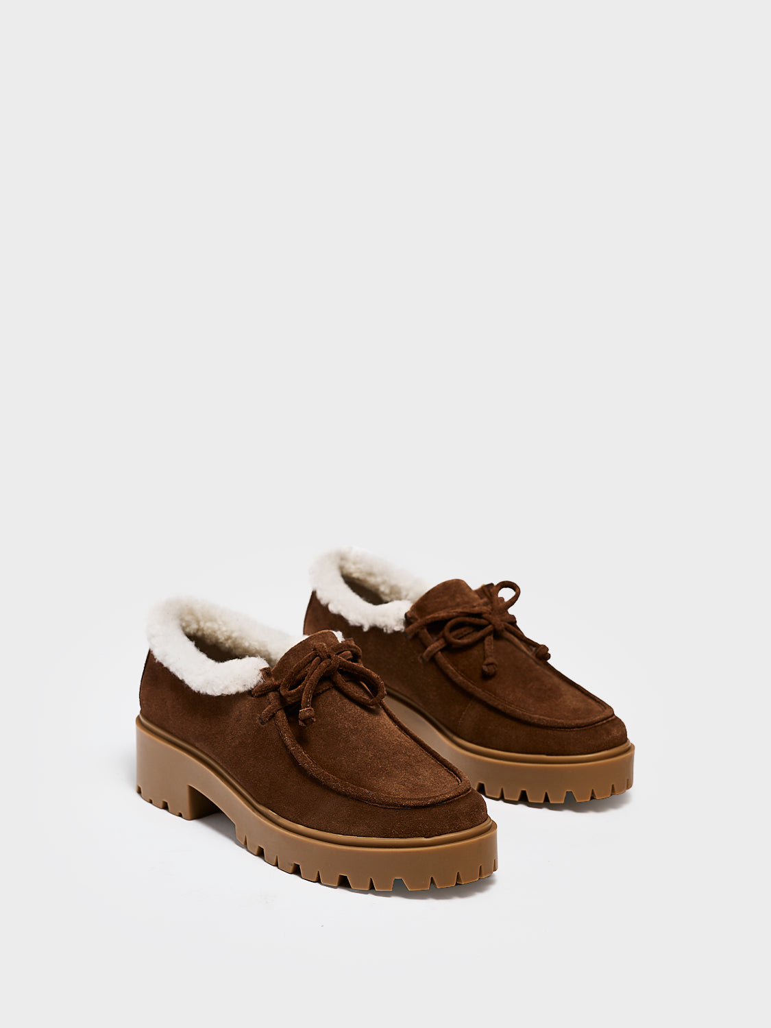 Angle view of a pair of mocha suede lug sole loafers with shearling lining and tie details.
