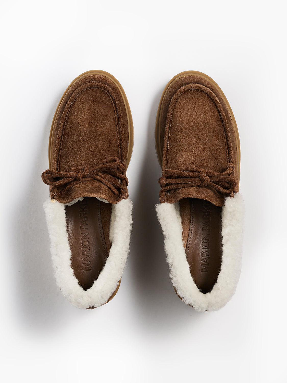 Top view of a pair of mocha suede lug sole loafers with shearling lining and tie details.