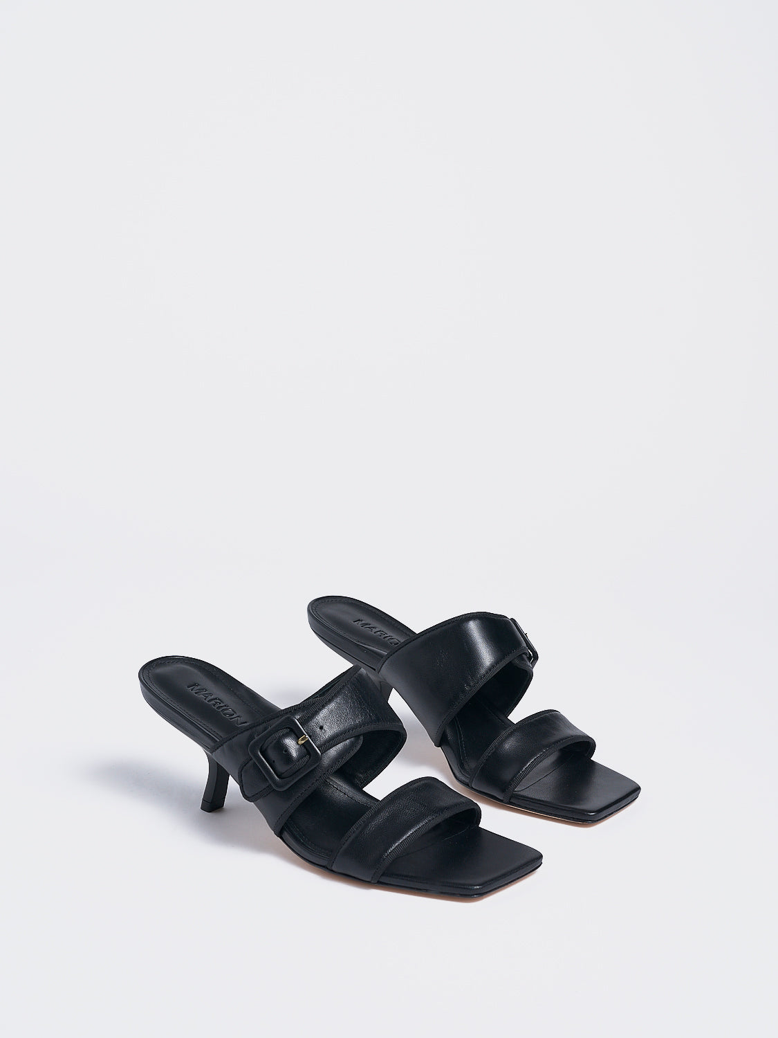 Angle view of a pair of black leather slide kitten heel sandals with a buckle detail.