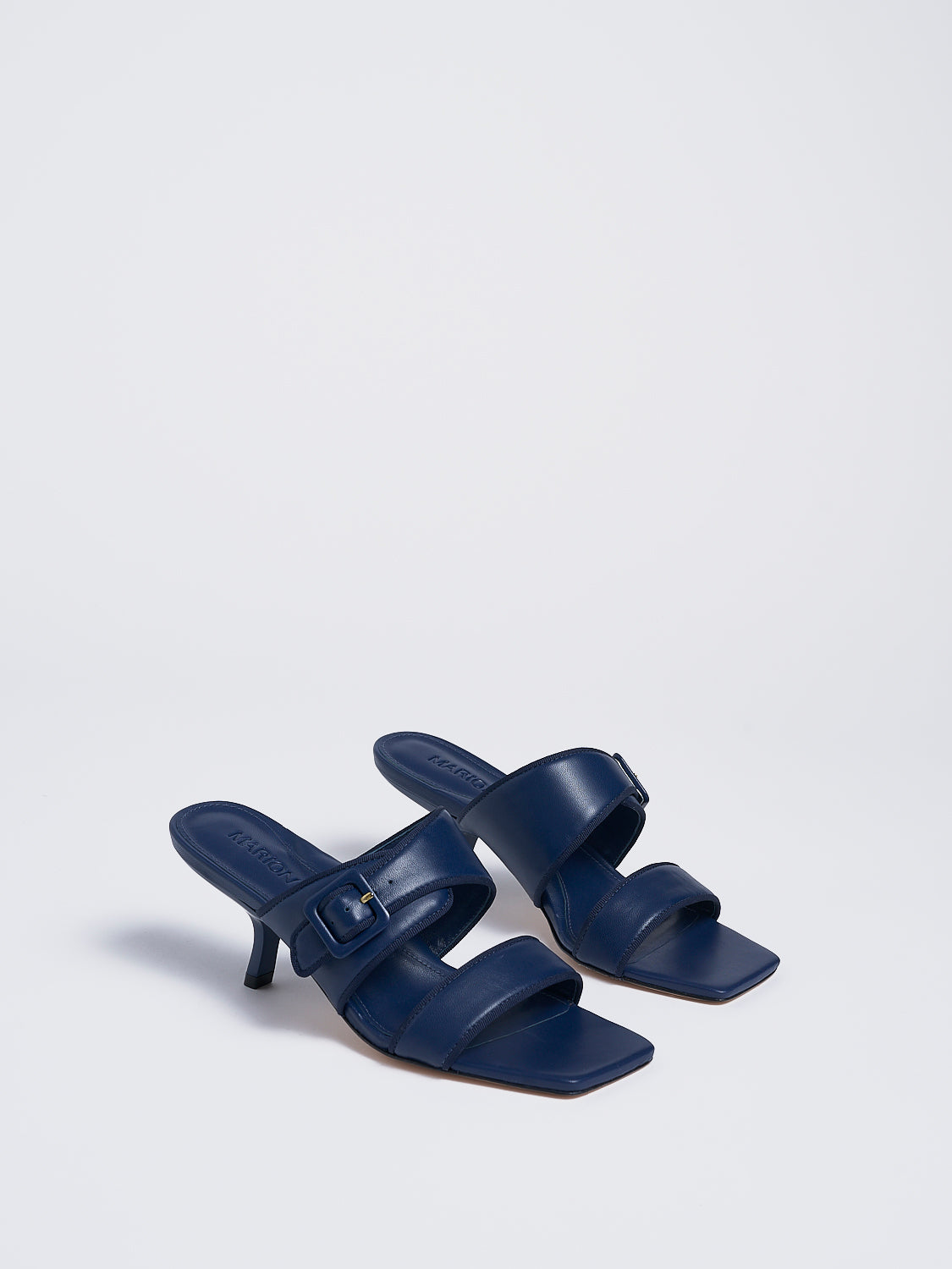 Angle view of a pair of navy leather slide kitten heel sandals with a buckle detail.