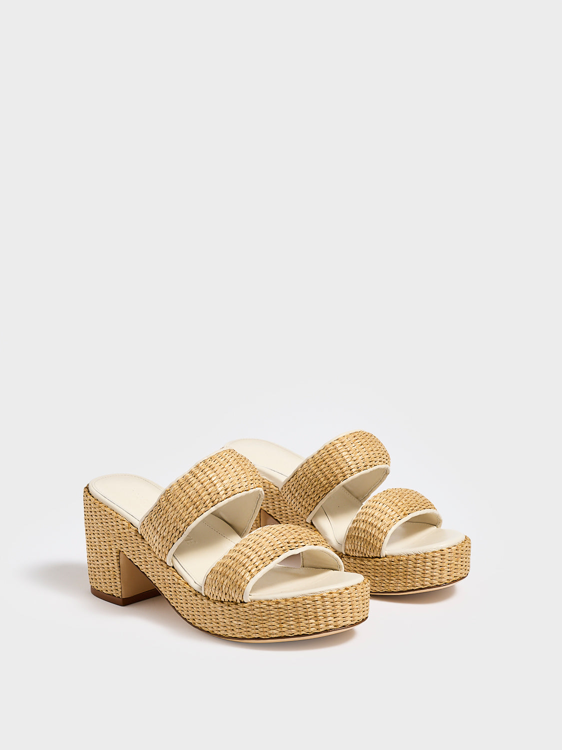 Angle view of a pair of raffia platform sandals with a light cream leather trim and puffed straps. 