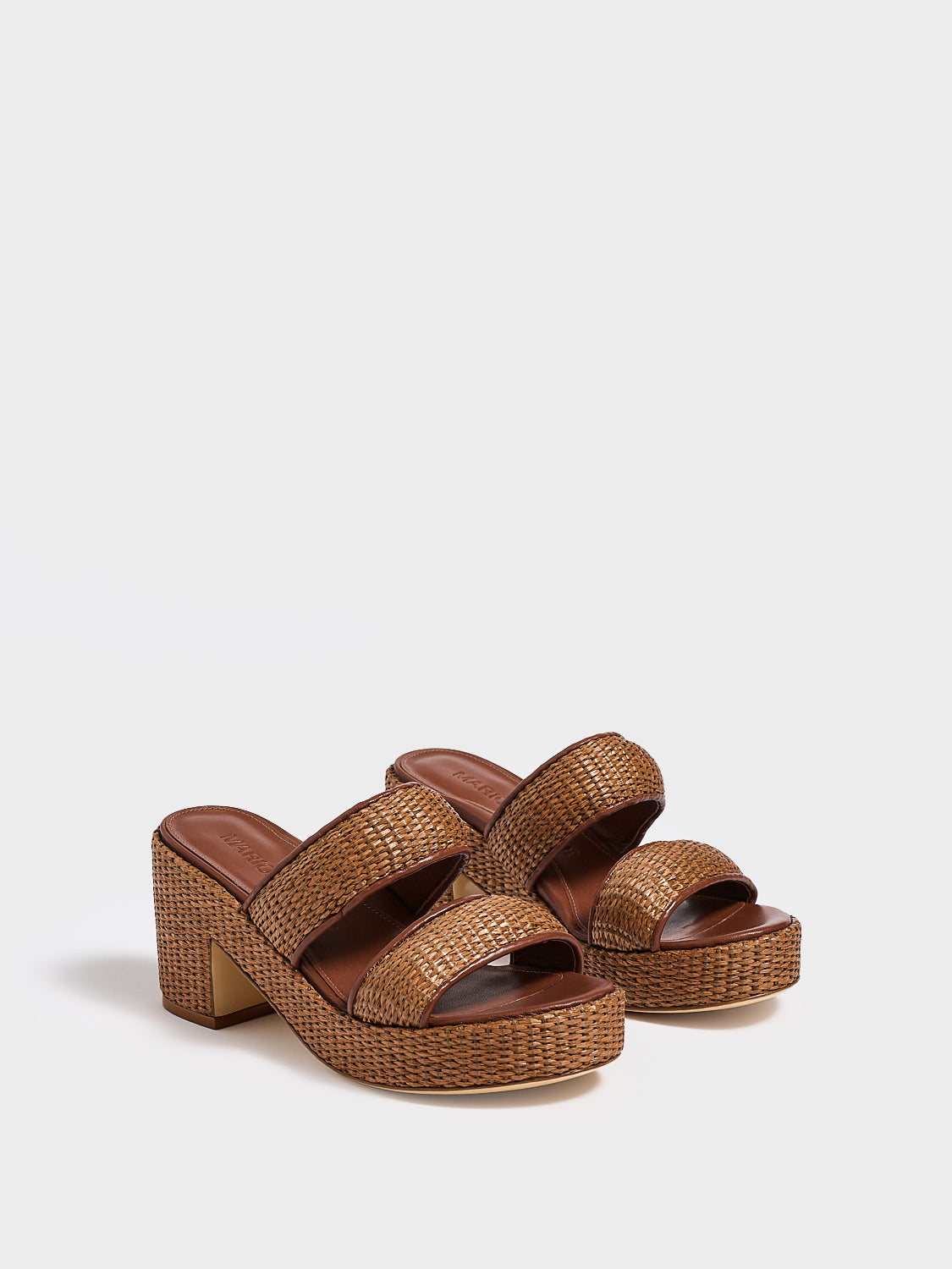 Angle view of a pair of dark brown raffia platform sandals with a  leather trim and puffed straps. 