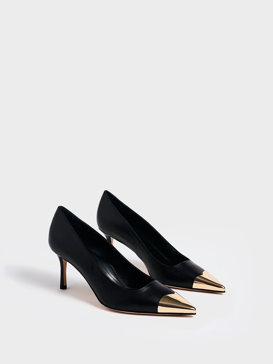 Angle view of a pair of black leather stiletto heel pumps with a gold metallic toe cap and a pointed toe.