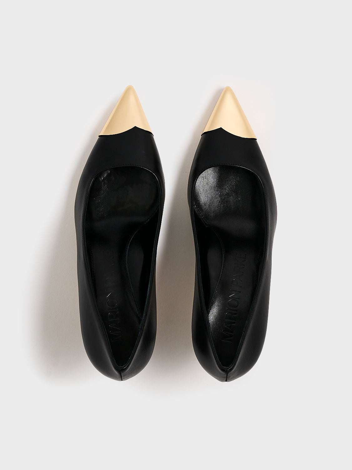 Top view of a pair of black leather stiletto heel pumps with a gold metallic toe cap and a pointed toe.