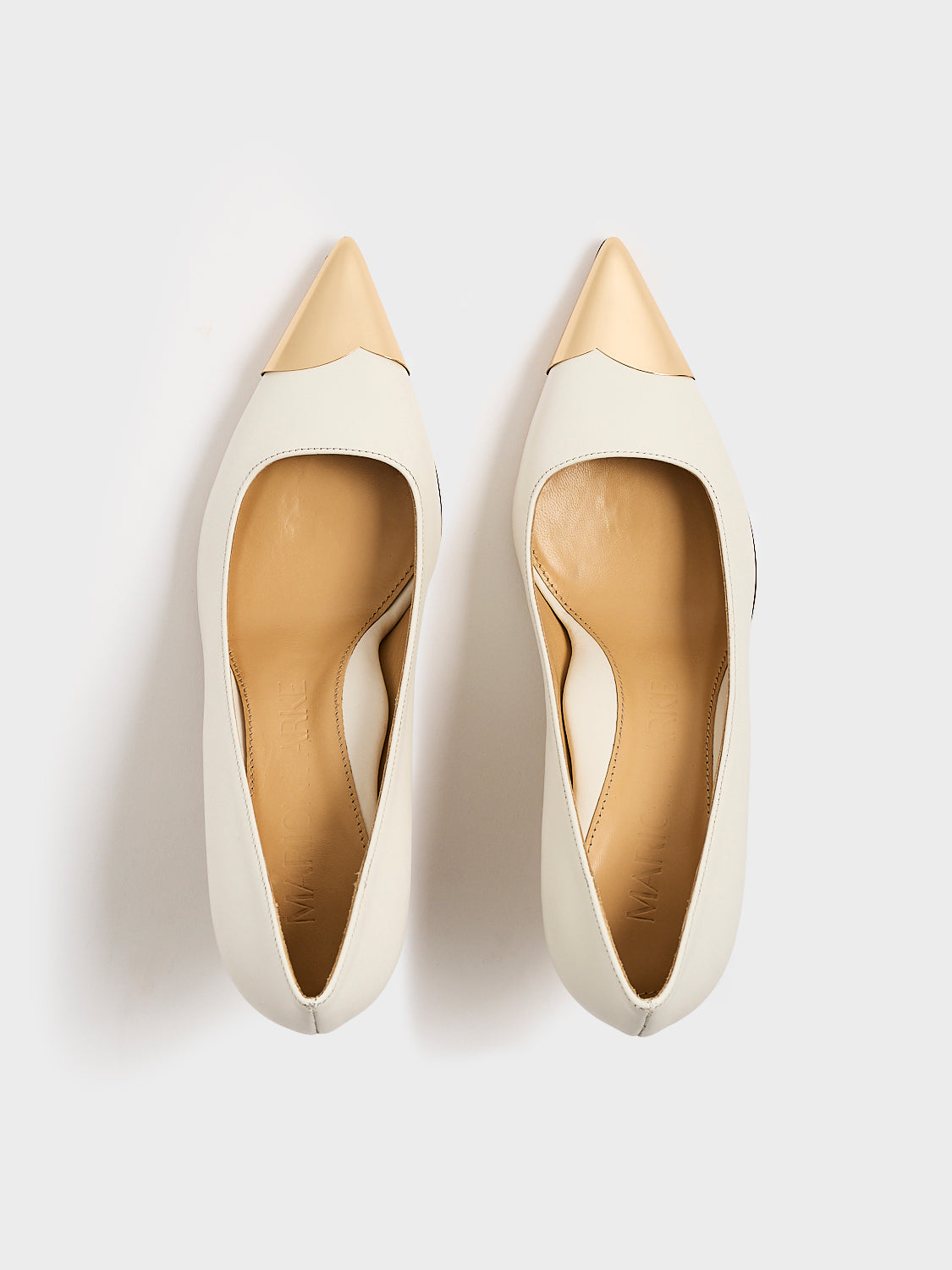 Top view of a pair of white leather stiletto heel pumps with a gold metallic toe cap and a pointed toe.