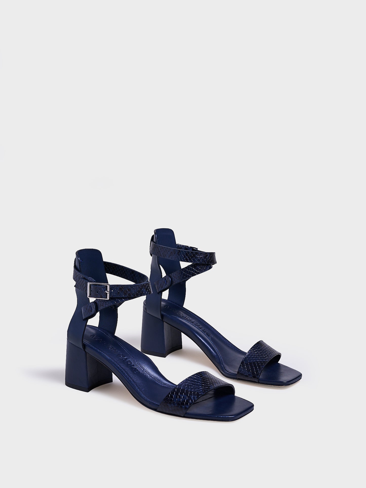 Angle View of a pair of navy python leather block heel sandals with an adjustable ankle strap design.