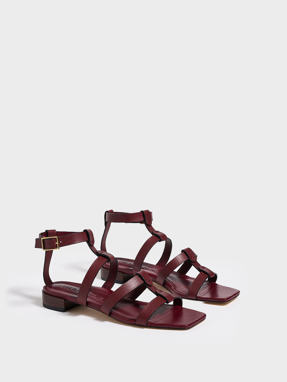 Angle view of a pair of burgundy leather gladiator sandals with an adjustable ankle strap.