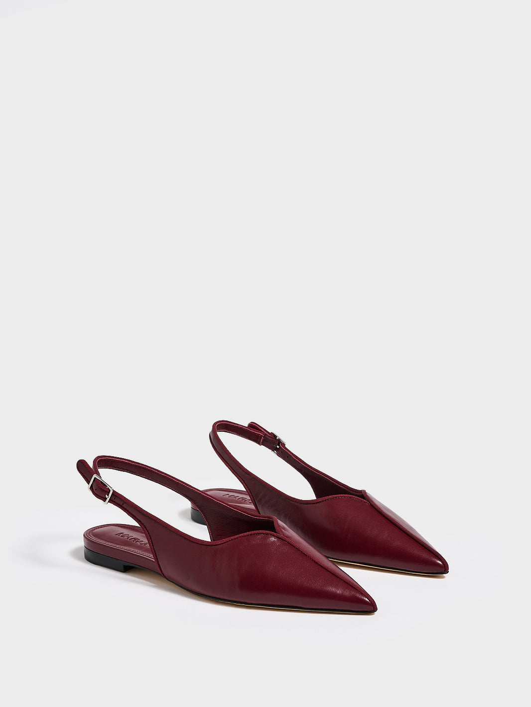 Angle view of a pair of burgundy leather slingback flats with a grosgrain trim detail.