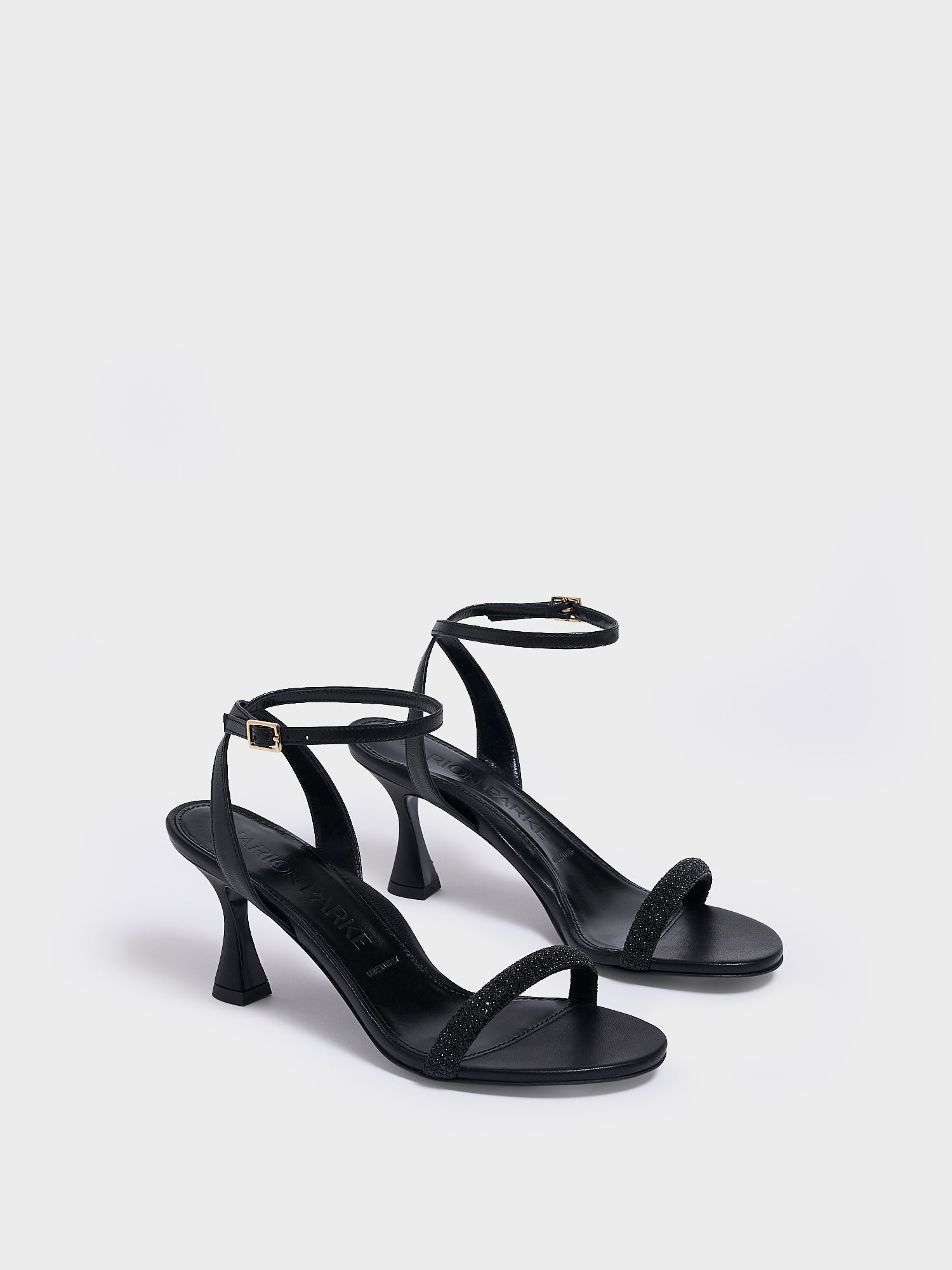 Angle view of a pair of black leather high heel sandals with a crystal embellished toe strap and adjustable ankle strap.