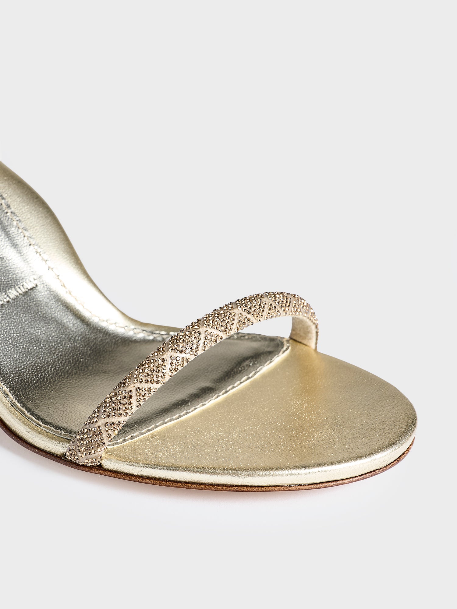Detail view of a pair of gold metallic leather high heel sandals with a crystal embellished toe strap and adjustable ankle strap.