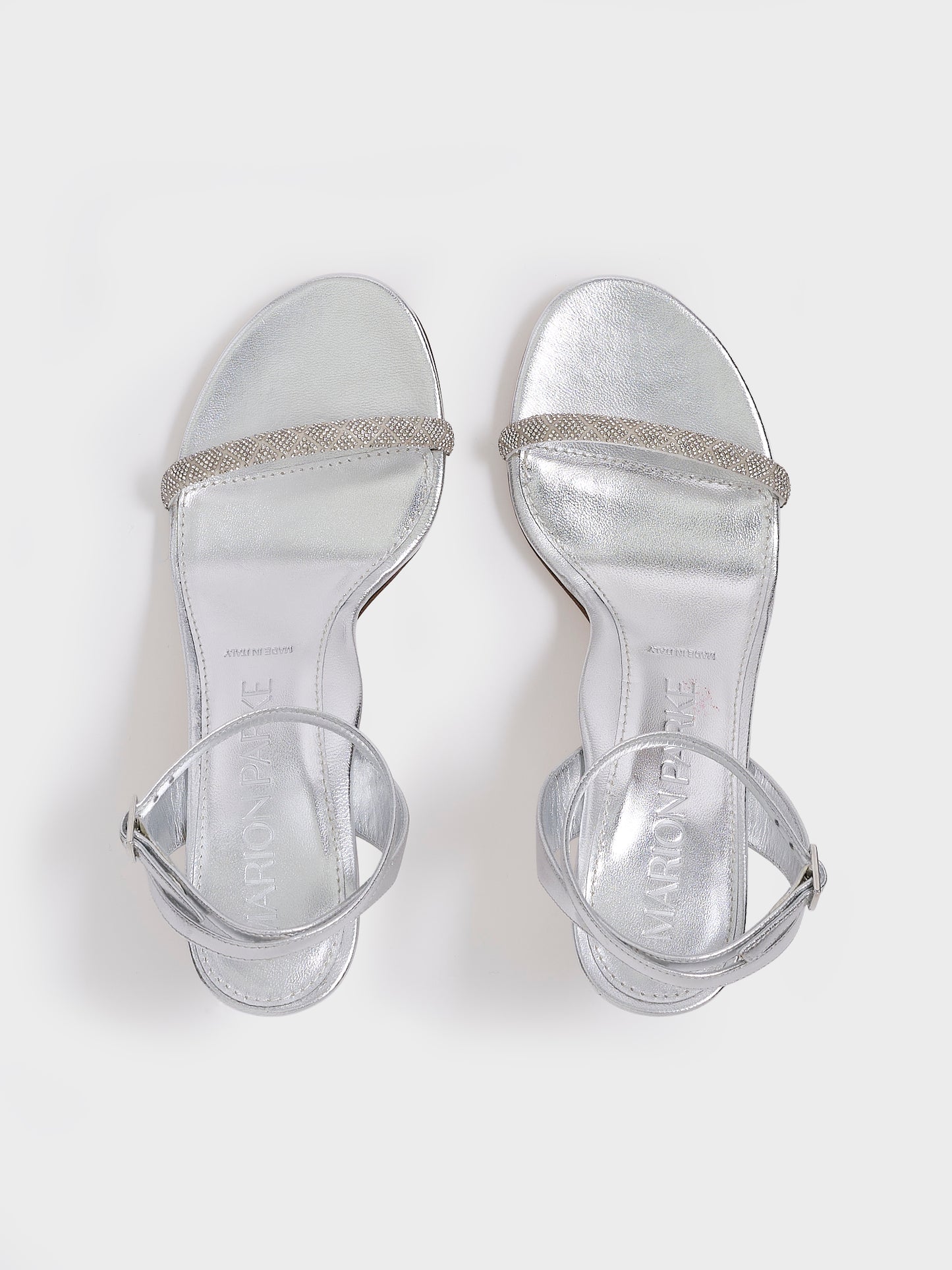 Top view of a pair of silver metallic leather high heel sandals with a crystal embellished toe strap and adjustable ankle strap.