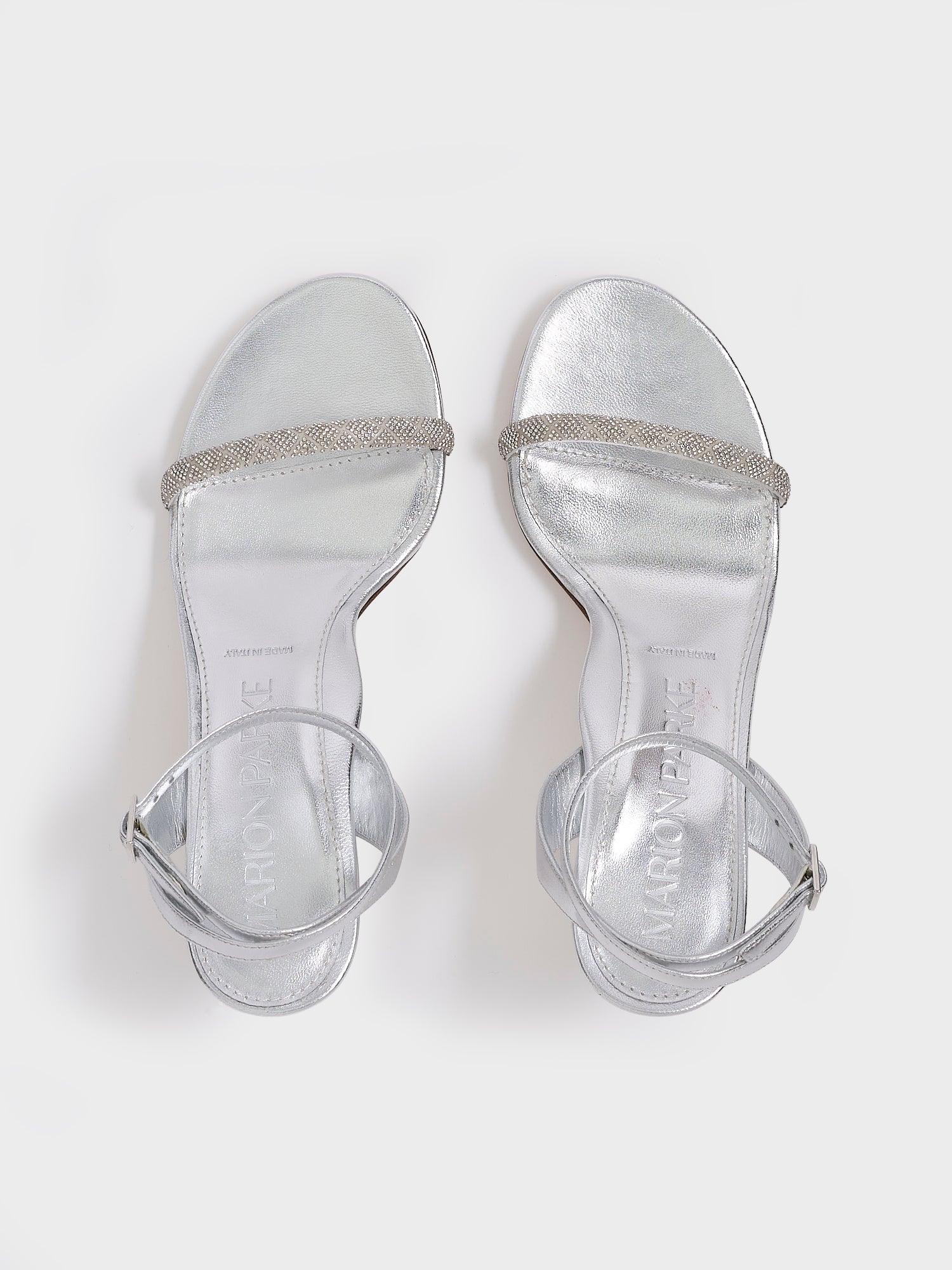 Top view of a pair of silver metallic leather high heel sandals with a crystal embellished toe strap and adjustable ankle strap.