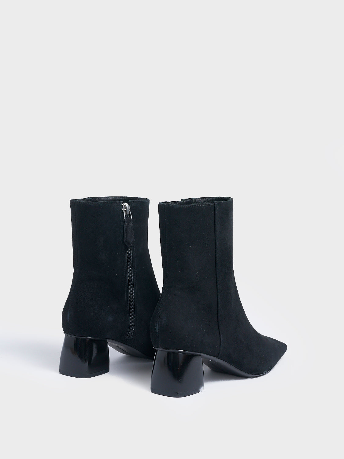 Back view of a pair of black suede ankle booties with a rounded heel shape, zipper closure, and square toe. 