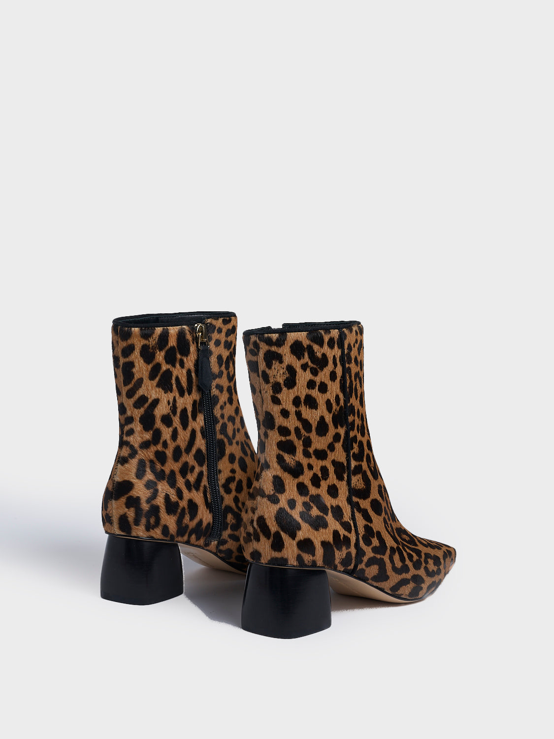 Back view of a pair of leopard hair calf ankle booties with a rounded heel shape, zipper closure, and square toe. 