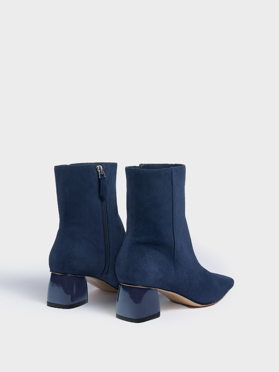 Back angle of a pair of navy suede ankle booties with a rounded heel shape, zipper closure, and square toe. 