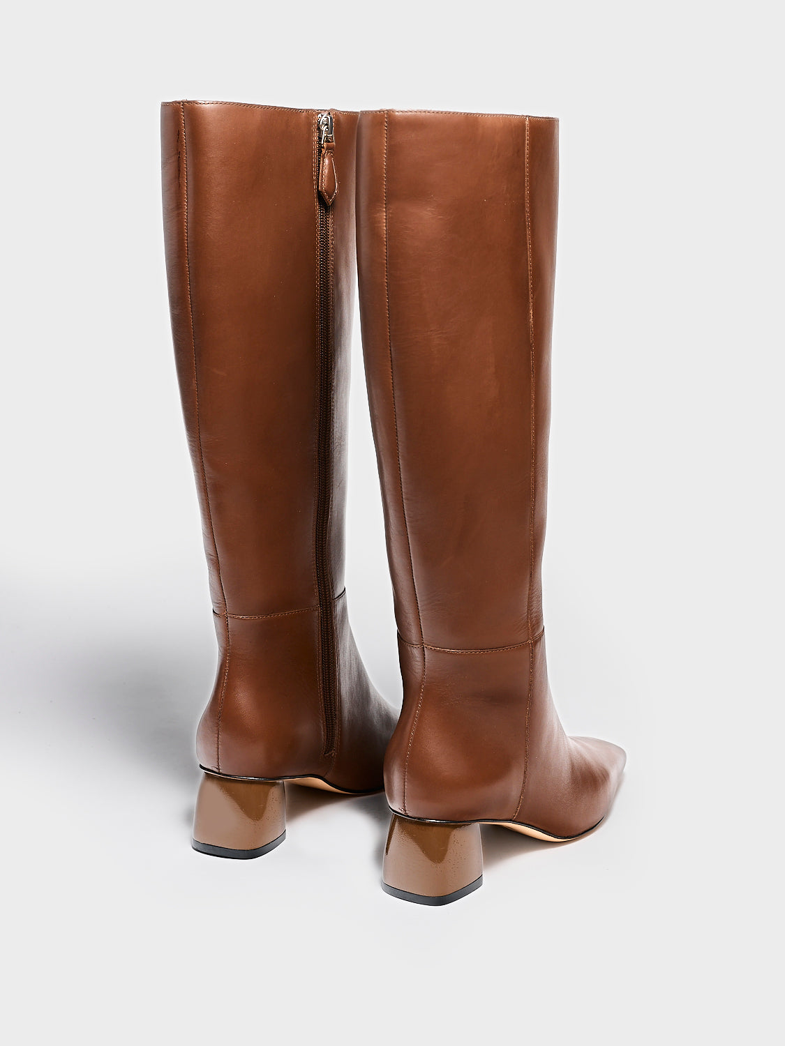 Back view of a pair of mocha brown nappa leather below the knee tall boots with a rounded heel shape, zipper closure, and square toe. 