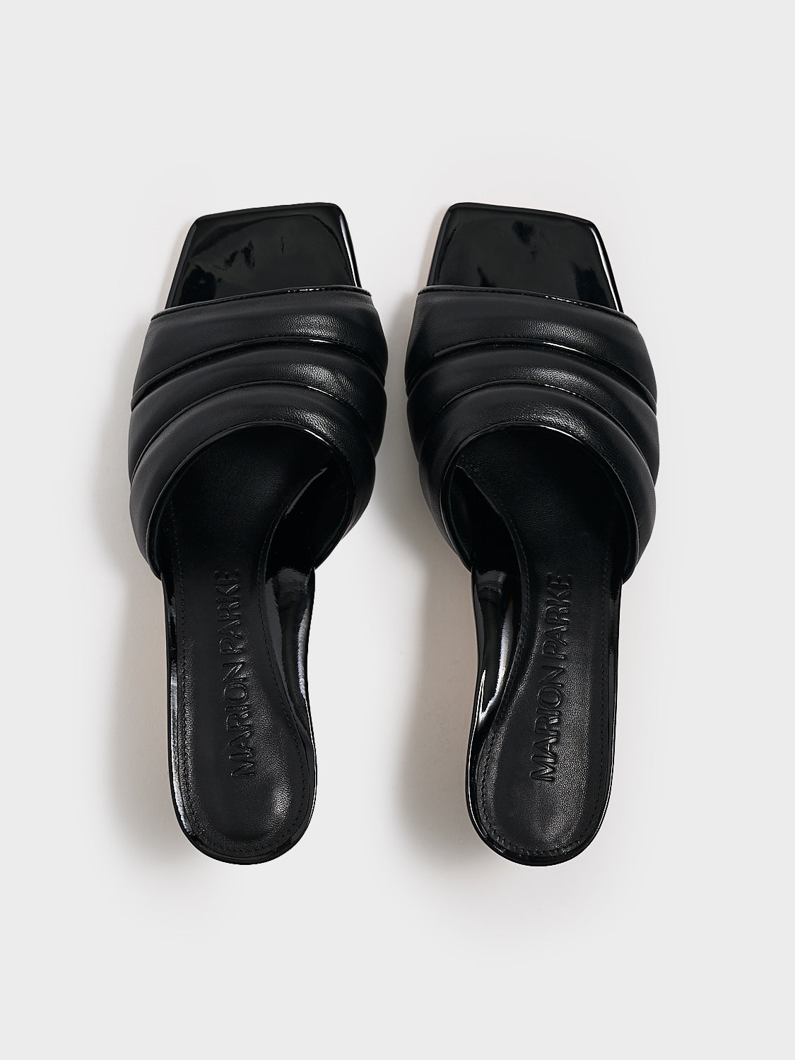 Top view of a pair of black leather slide kitten heels with a patent leather trimmed puffy strap detail.