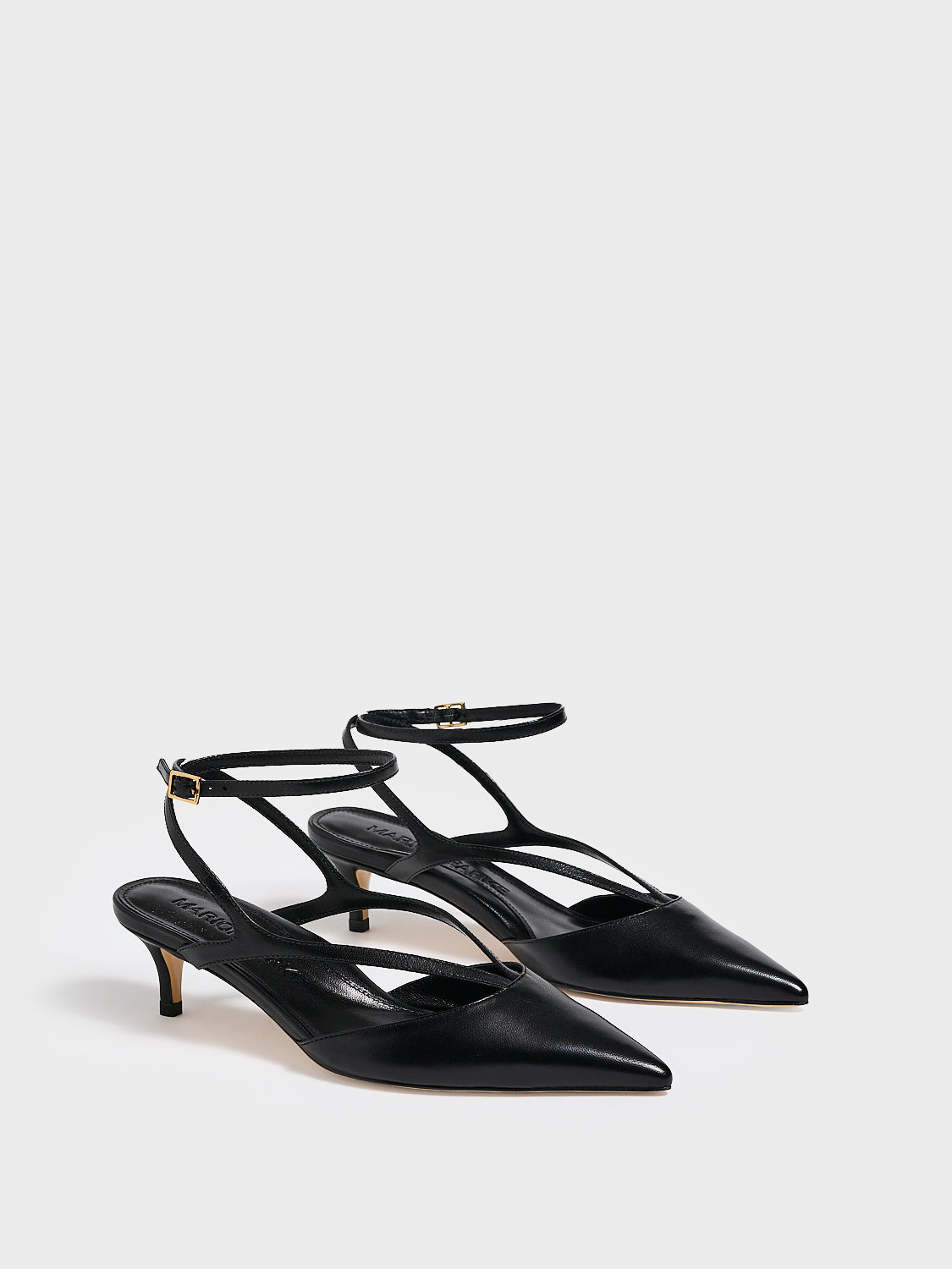 Angle view of a pair of black leather kitten heels with sculpted strap design and an adjustable ankle strap.