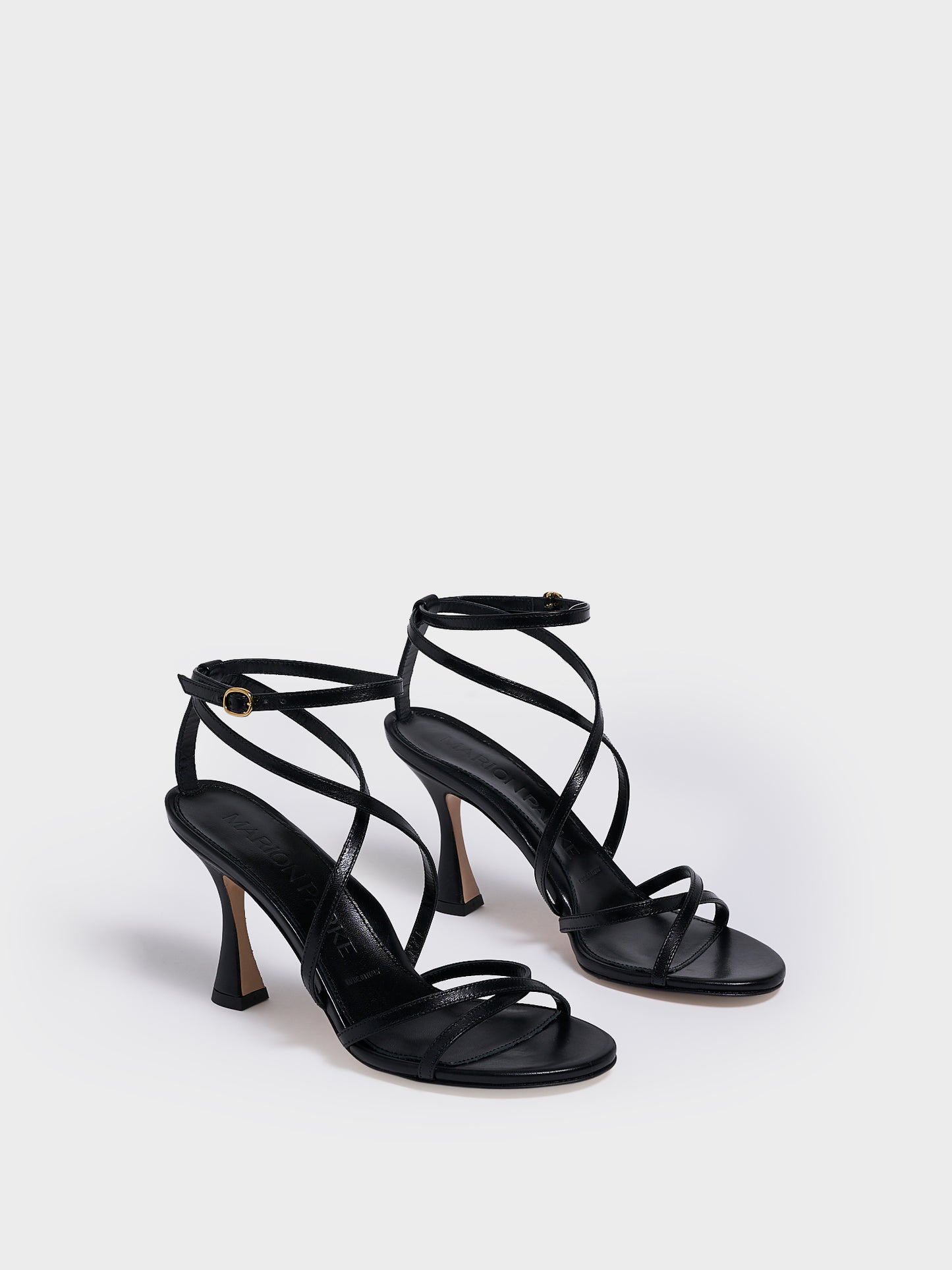 Angle view of a black leather high heel strappy sandal with an ankle strap detail. 