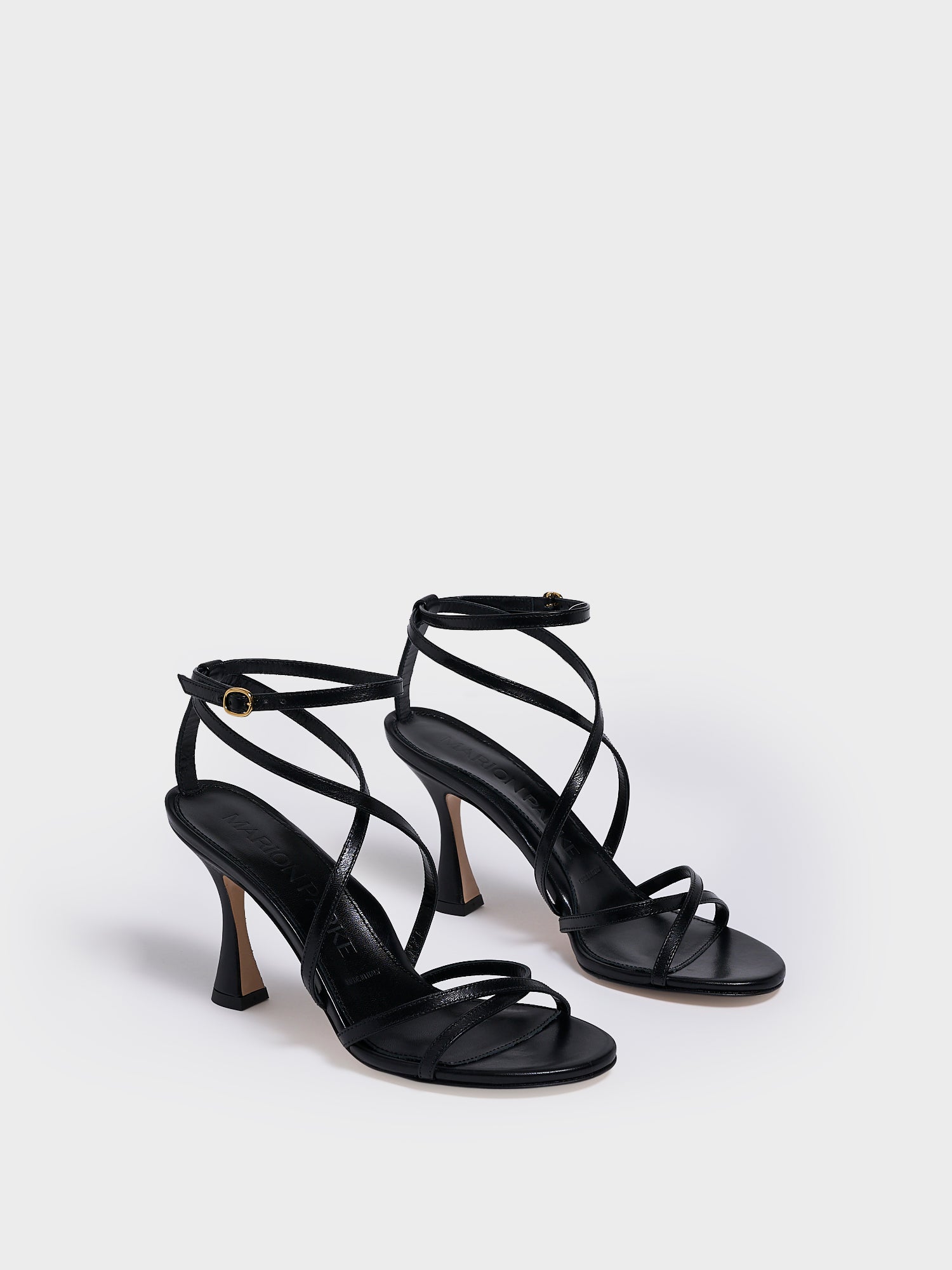 Angle view of a black leather high heel strappy sandal with an ankle strap detail. 