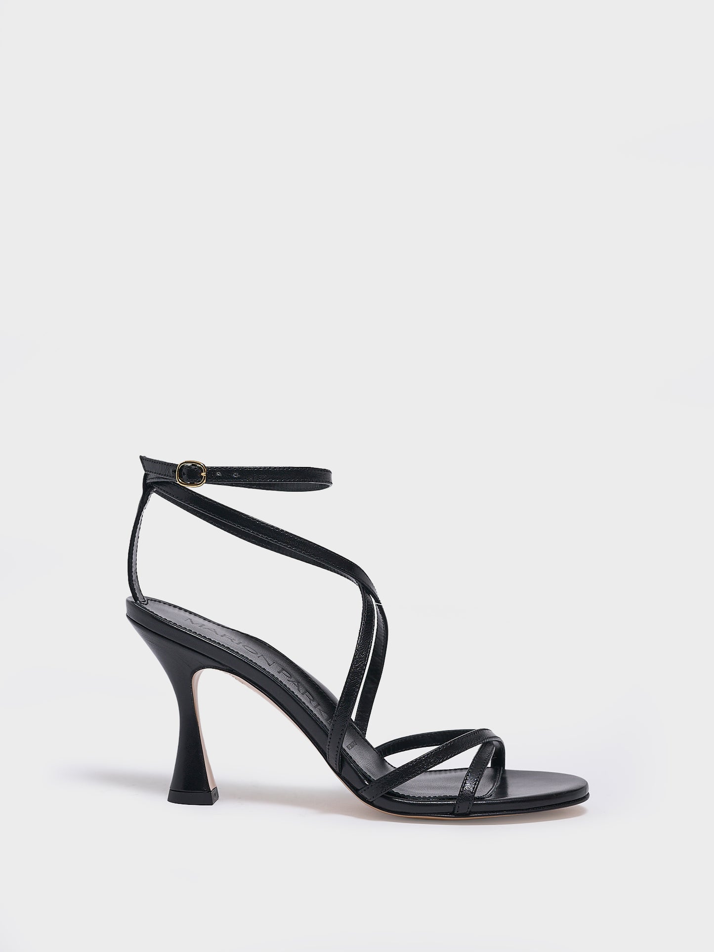 Profile view of a black leather high heel strappy sandal with an ankle strap detail. 
