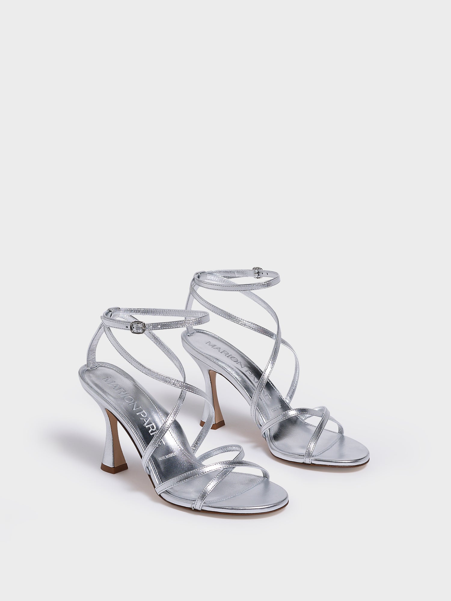 angle view of a silver leather high heel strappy sandal with an ankle strap detail. 