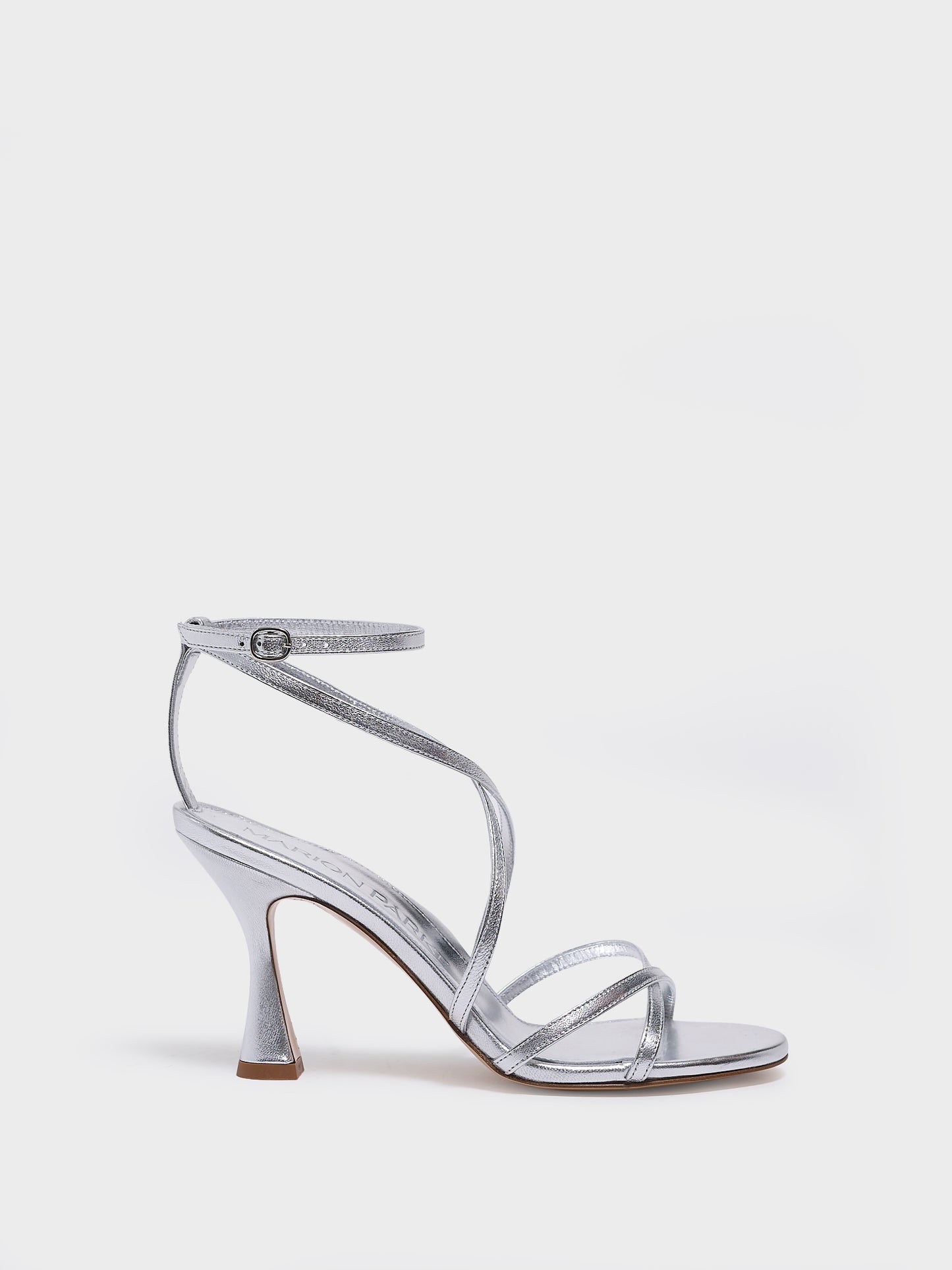 Profile view of a silver leather high heel strappy sandal with an ankle strap detail. 