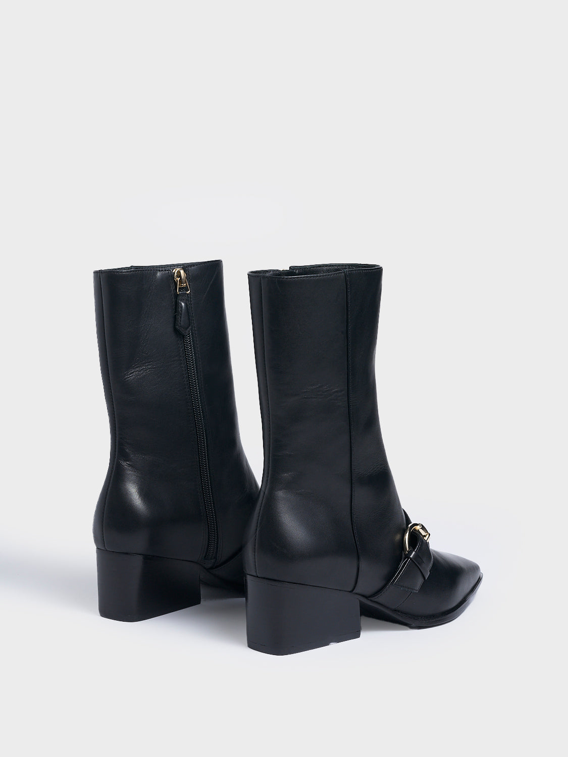 Back view of a pair black nappa leather  ankle booties with a zipper closure, silver buckle, and block heel. 