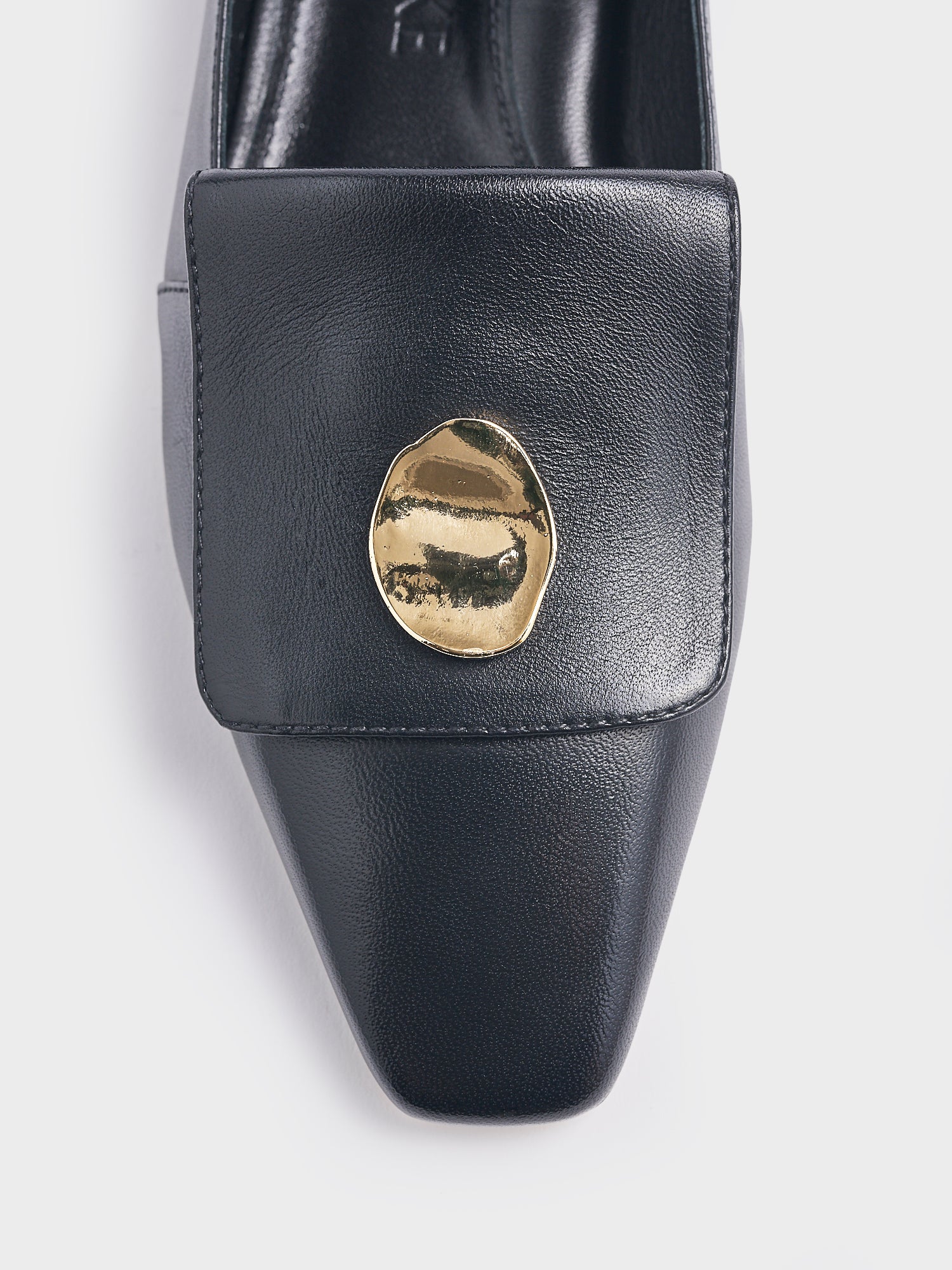 Detail view of a black leather loafer with gold hardware. 