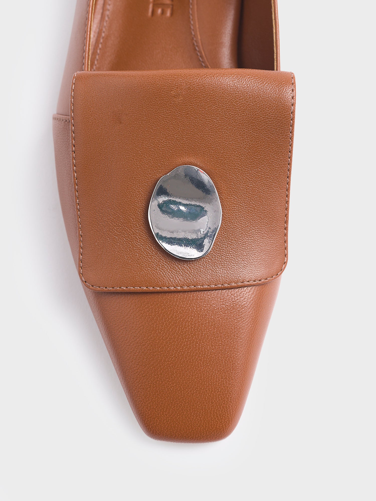 Detail view of a chestnut leather loafer with silver hardware. 