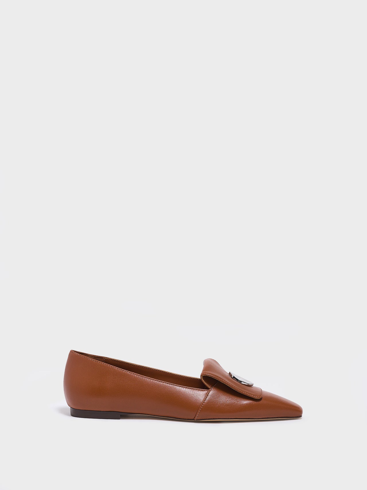 Profile view of a chestnut leather  flat loafer with a  silver hardware detail and squared toe. 