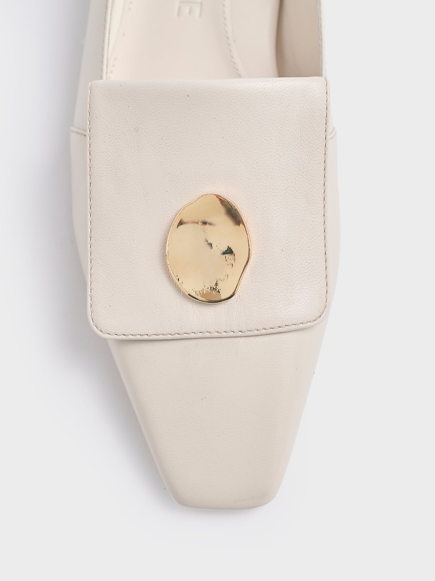 Detail view of an ivory leather loafer with gold hardware. 