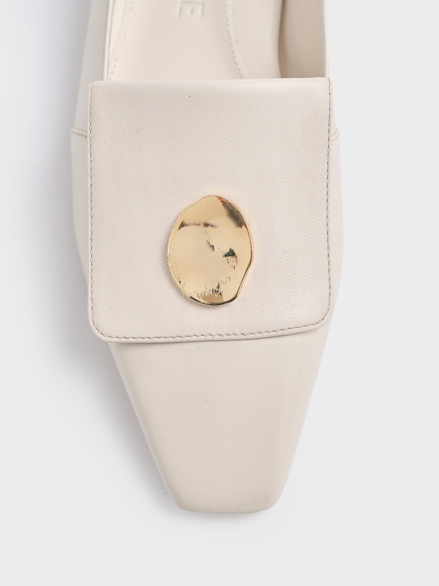 Detail view of an ivory leather loafer with gold hardware. 