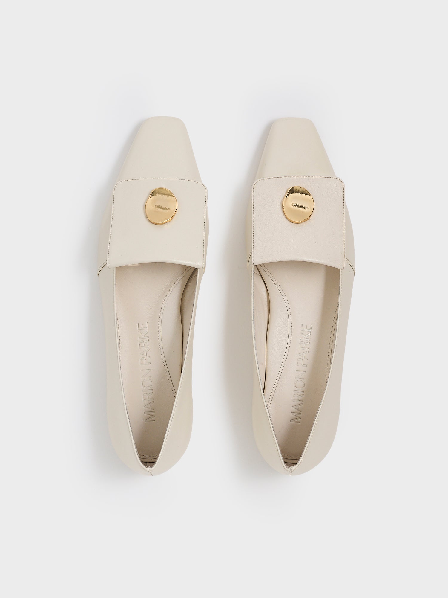 Top view of a pair of ivory leather  flat loafers with a  gold hardware detail and squared toe. 