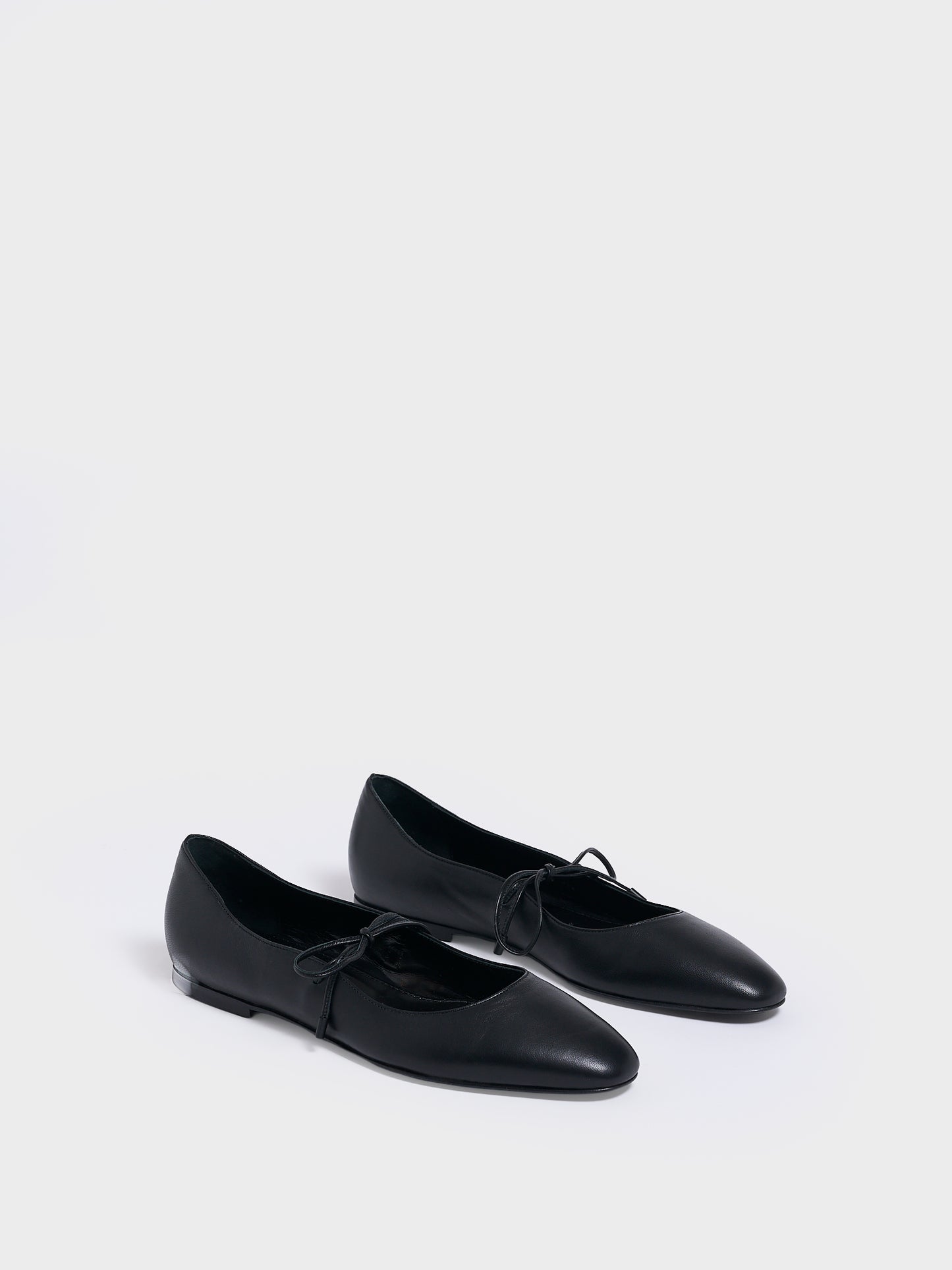 Angle view of a pair of black leather ballet flats with an almond toe and tie detail.