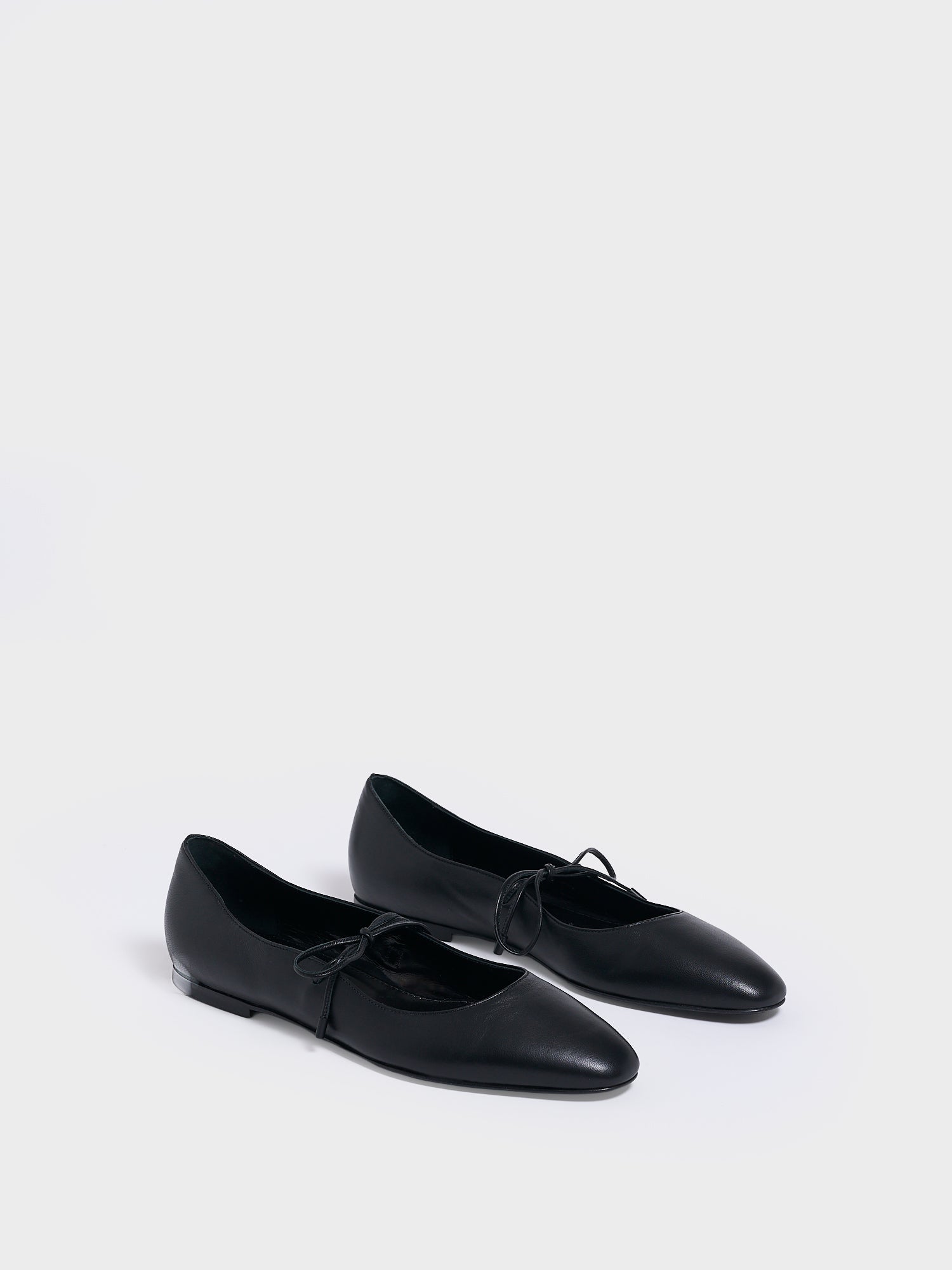 Angle view of a pair of black leather ballet flats with an almond toe and tie detail.