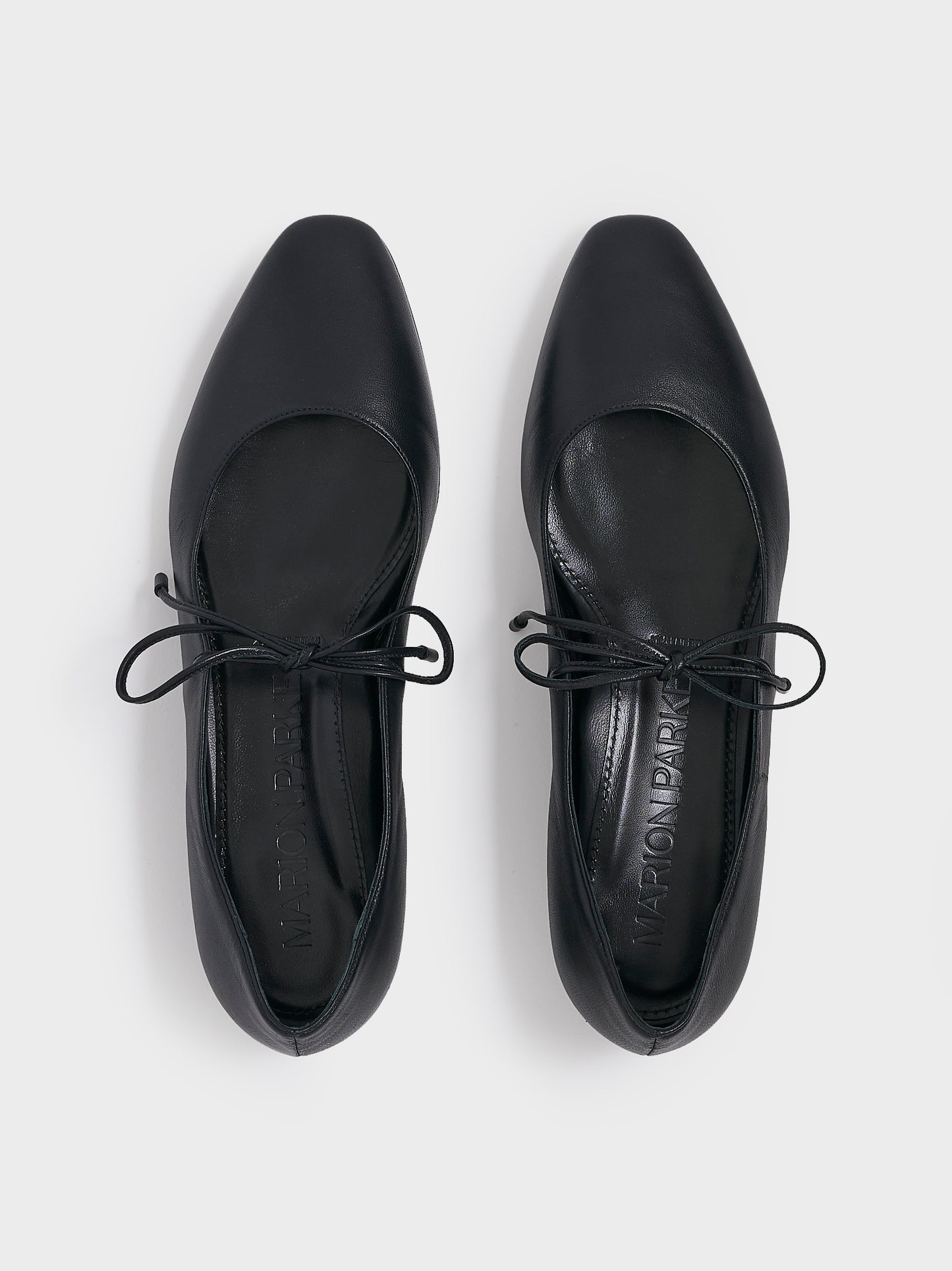 Top view of a pair of black leather ballet flats with an almond toe and tie detail.