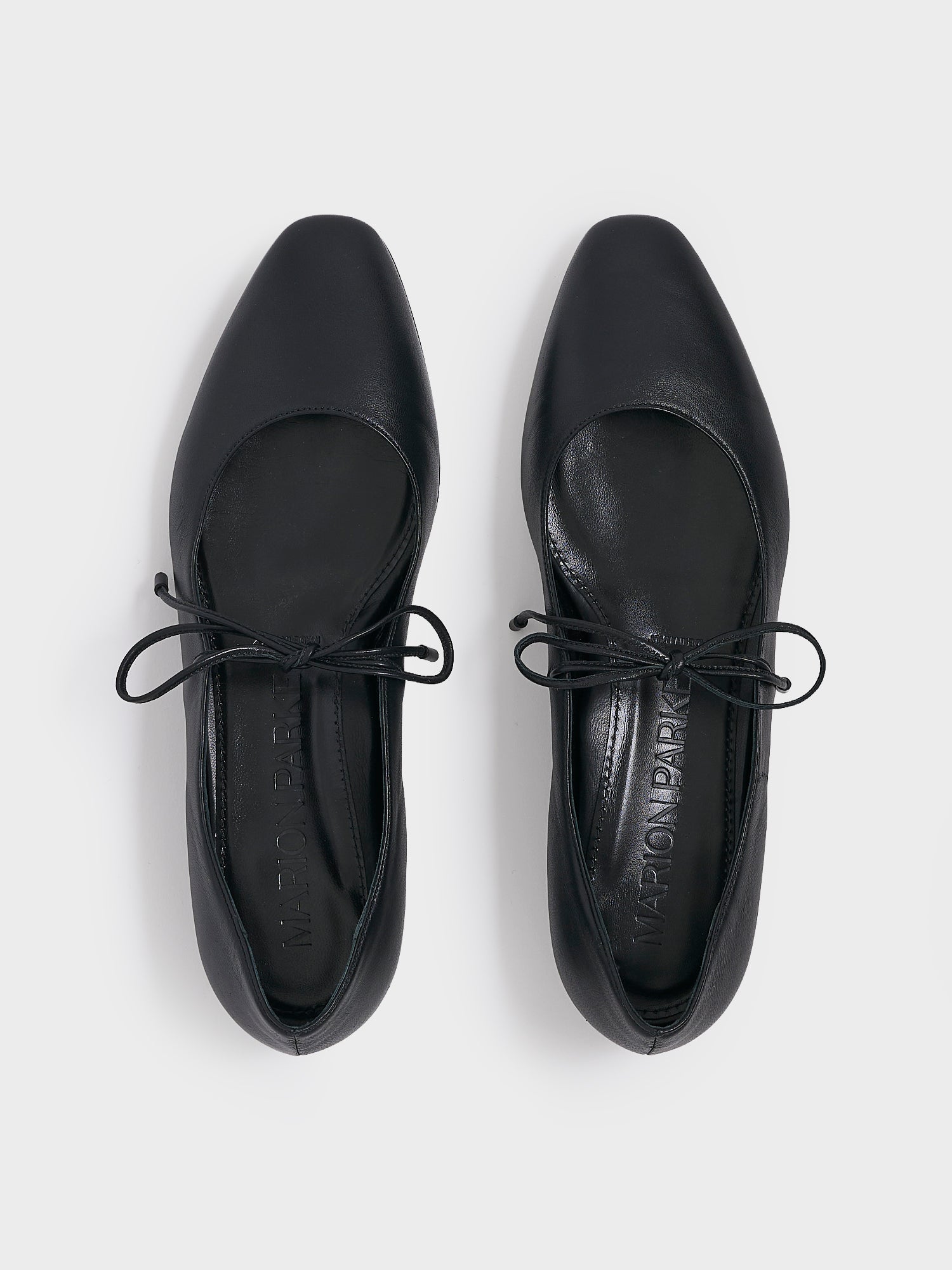 Top view of a pair of black leather ballet flats with an almond toe and tie detail.