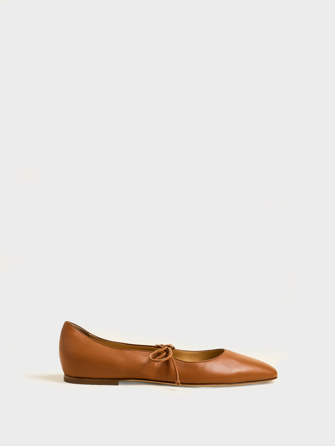 Profile view of a chestnut suede ballet flat with an almond toe and tie detail.