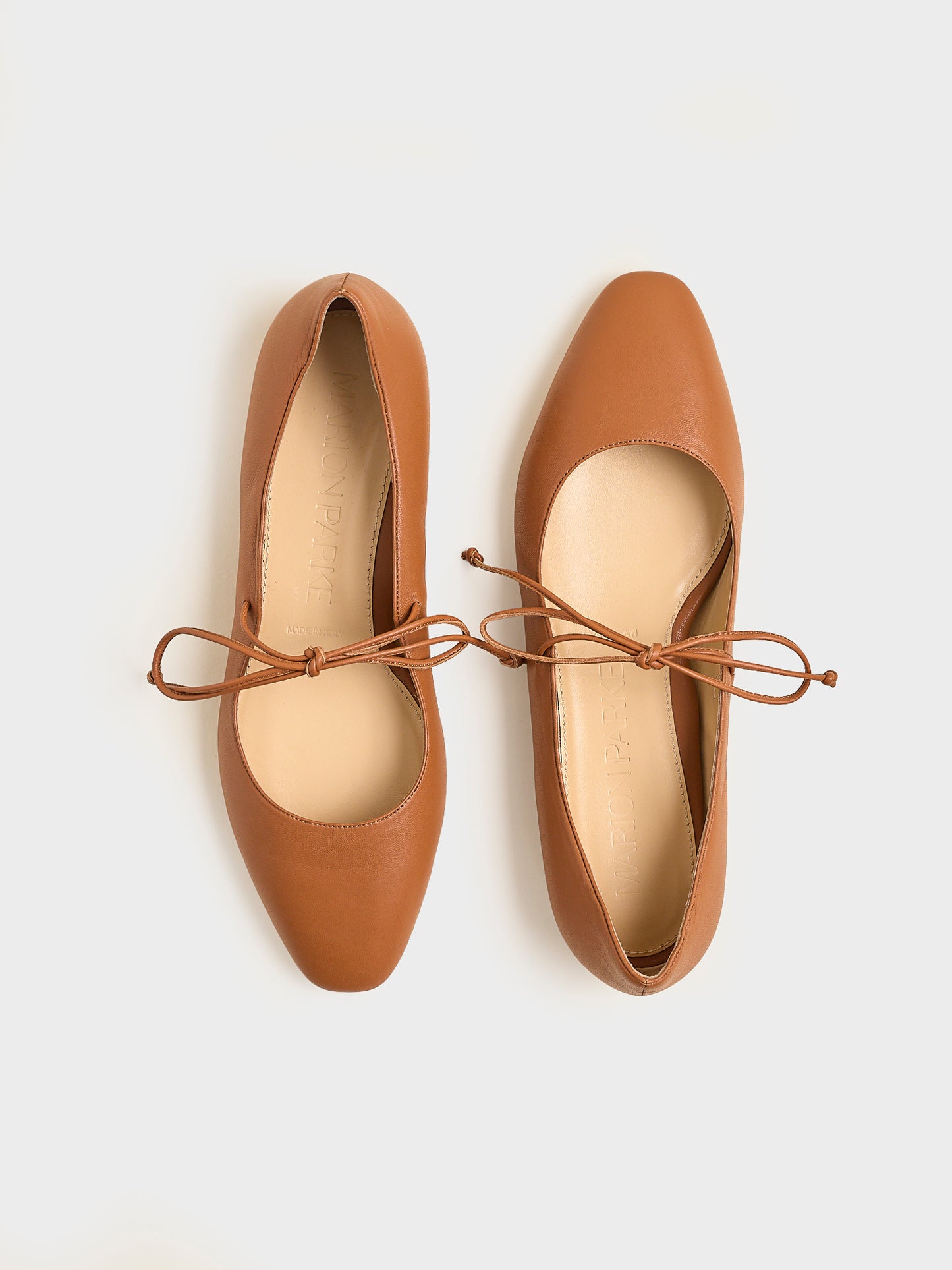 Top view of a pair of chestnut suede ballet flats with an almond toe and tie detail.
