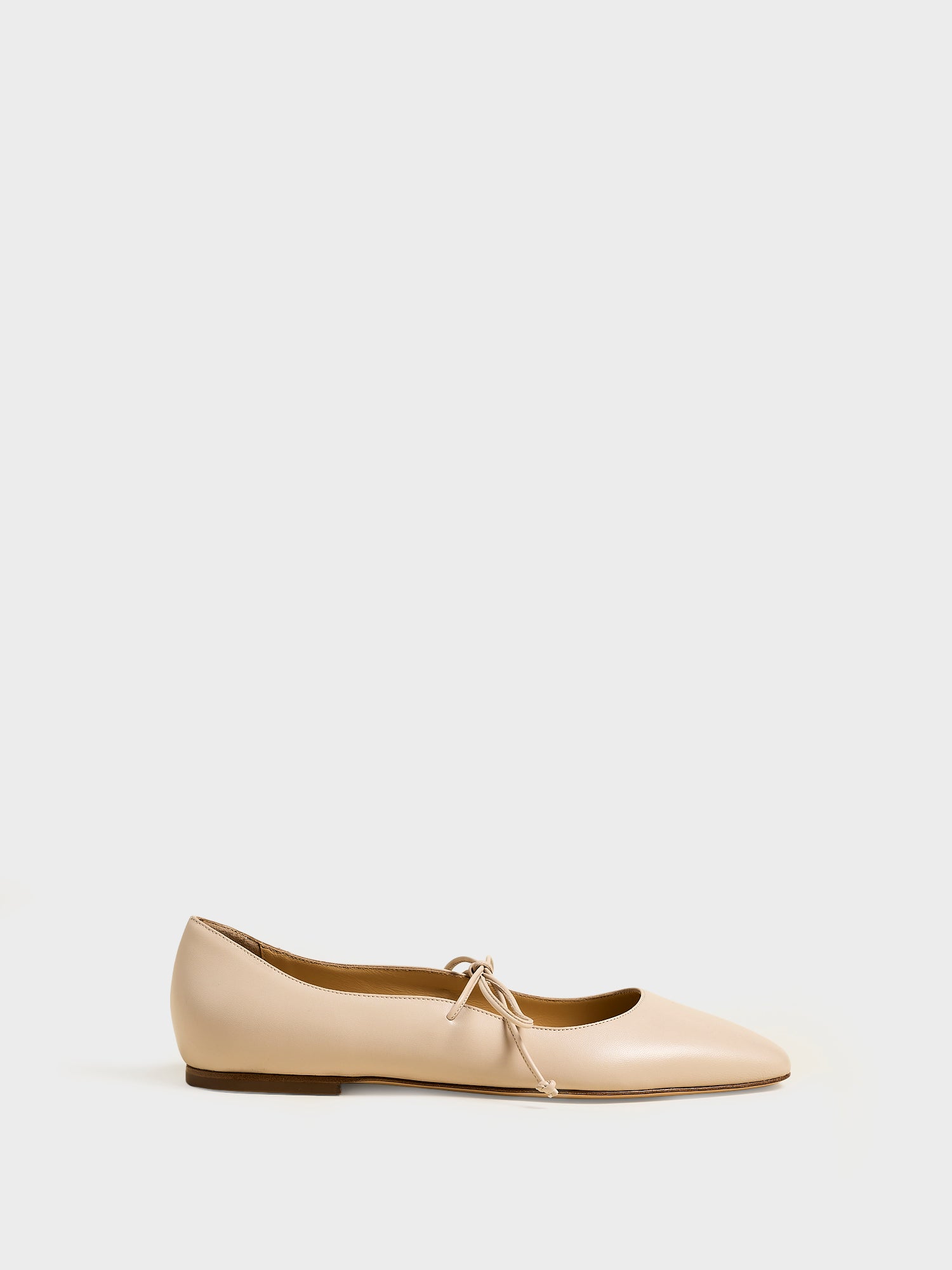 Profile view of a sand leather ballet flat with an almond toe and tie detail.