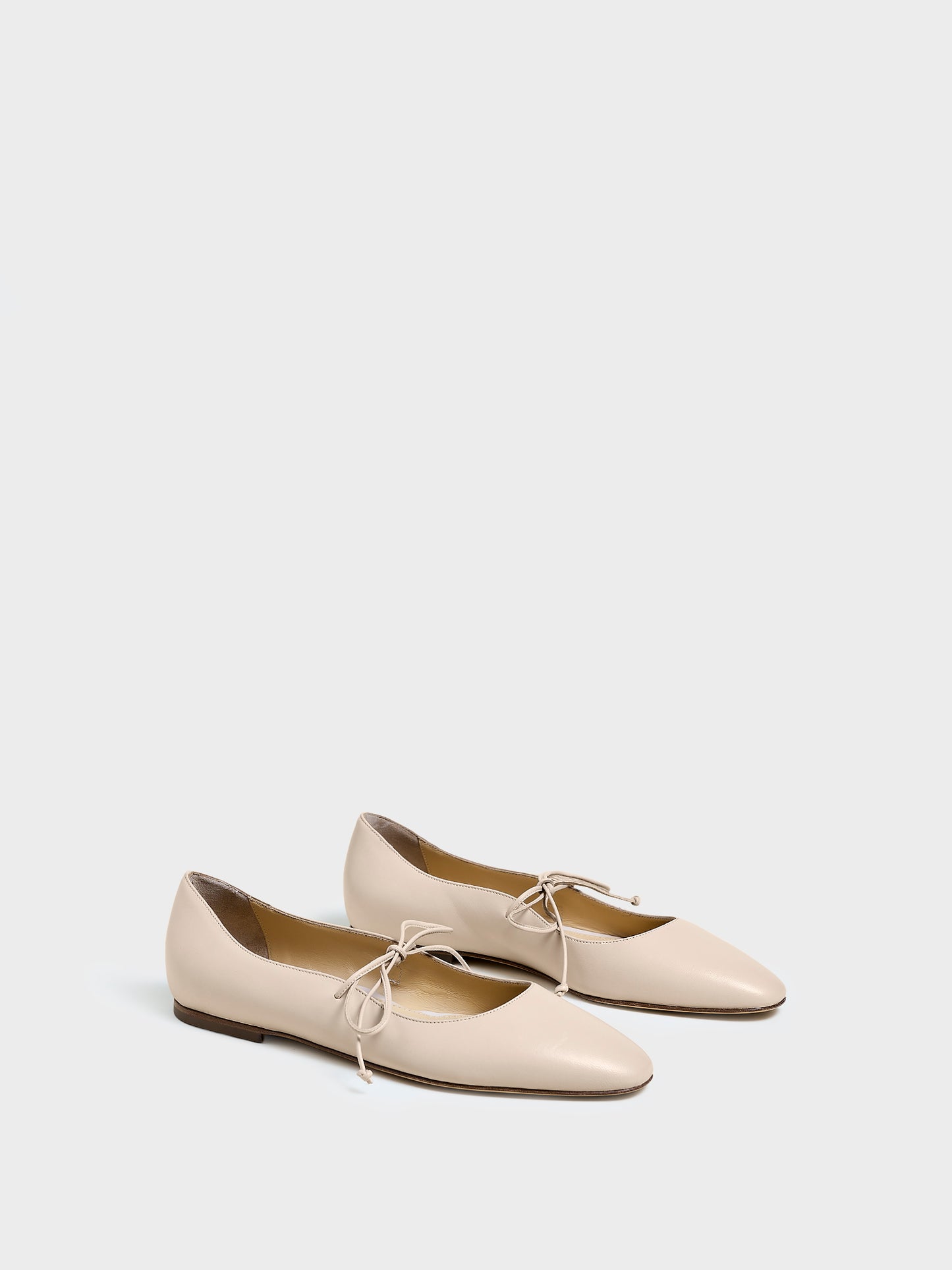 Angle view of a pair of sand leather ballet flats with an almond toe and tie detail.
